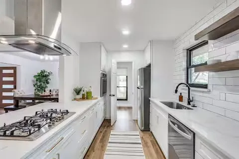Galley kitchen featuring a gas cooktop, stainless steel range hood, built-in oven, and a single basin sink with a matte black faucet