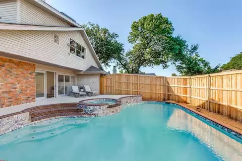 Outdoor swimming pool with integrated spa, surrounded by a wood privacy fence and brick-accented patio