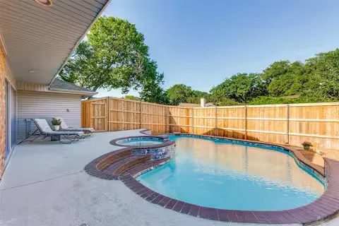Outdoor pool with integrated hot tub, surrounded by a concrete patio and a wooden privacy fence