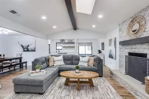Vaulted ceiling with exposed beam, recessed lighting, wood-finish flooring, stone fireplace with hearth, and skylight