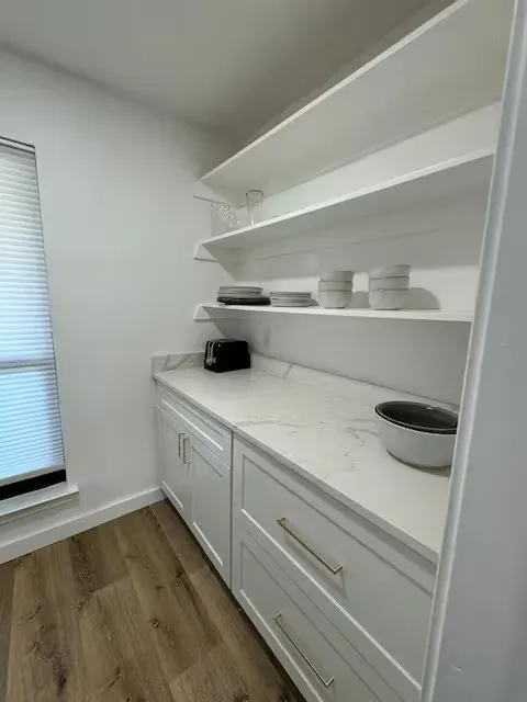 White flat-panel cabinetry with gold-tone hardware, wood-finish flooring, white countertop, and open shelving