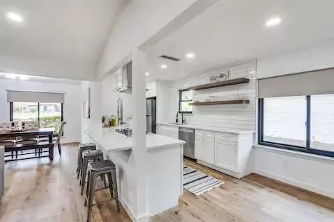 Wood-finish flooring throughout, white cabinetry, white countertop, stainless steel appliances, and white subway tile backsplash