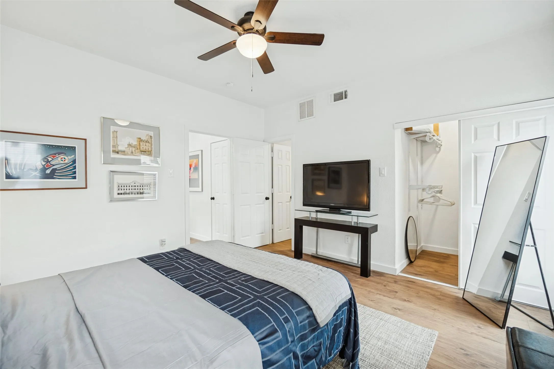 White walls with wood-finish flooring, ceiling fan with integrated lighting, and multiple panel doors