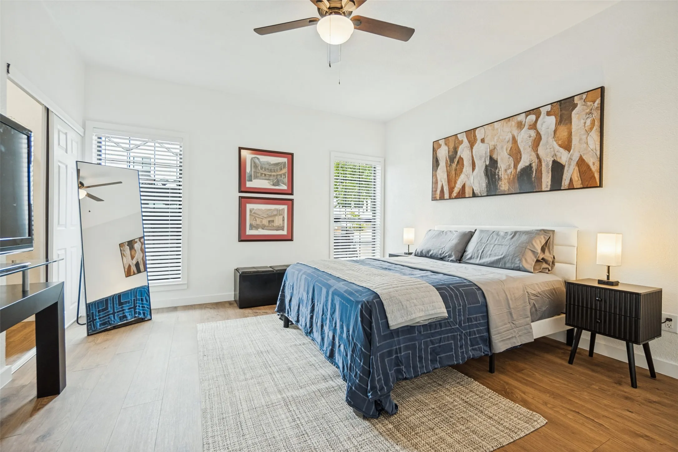 Wood-finish flooring throughout, white walls, two windows with blinds, and a ceiling fan with light fixture