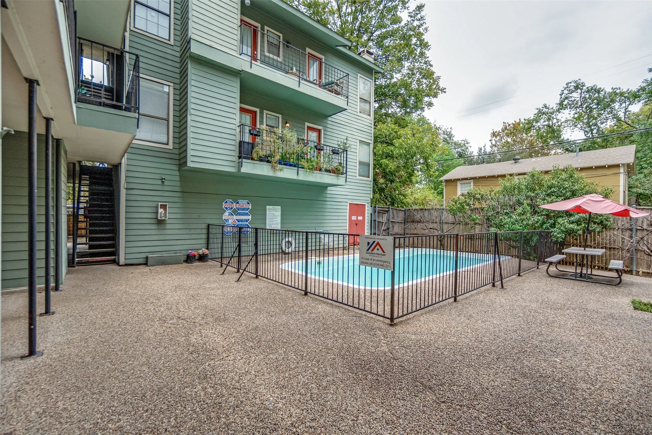 Fenced swimming pool with concrete patio surround and adjacent building featuring multiple balconies