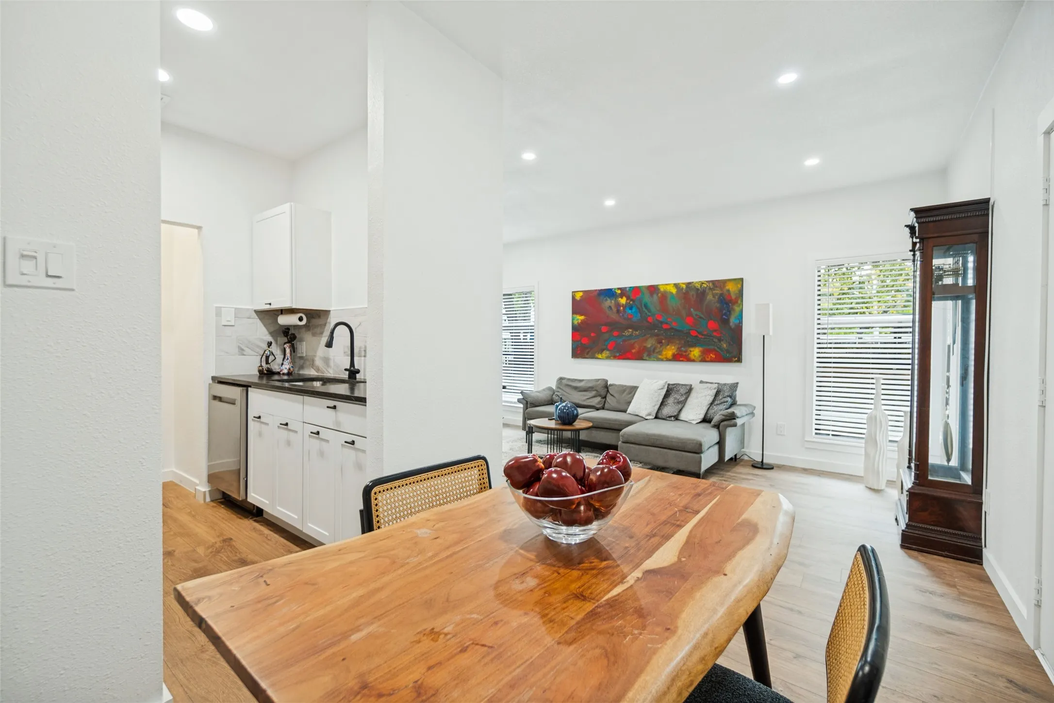 Recessed lighting, wood-finish flooring, white cabinetry, stainless steel dishwasher, and a dark countertop with a black faucet