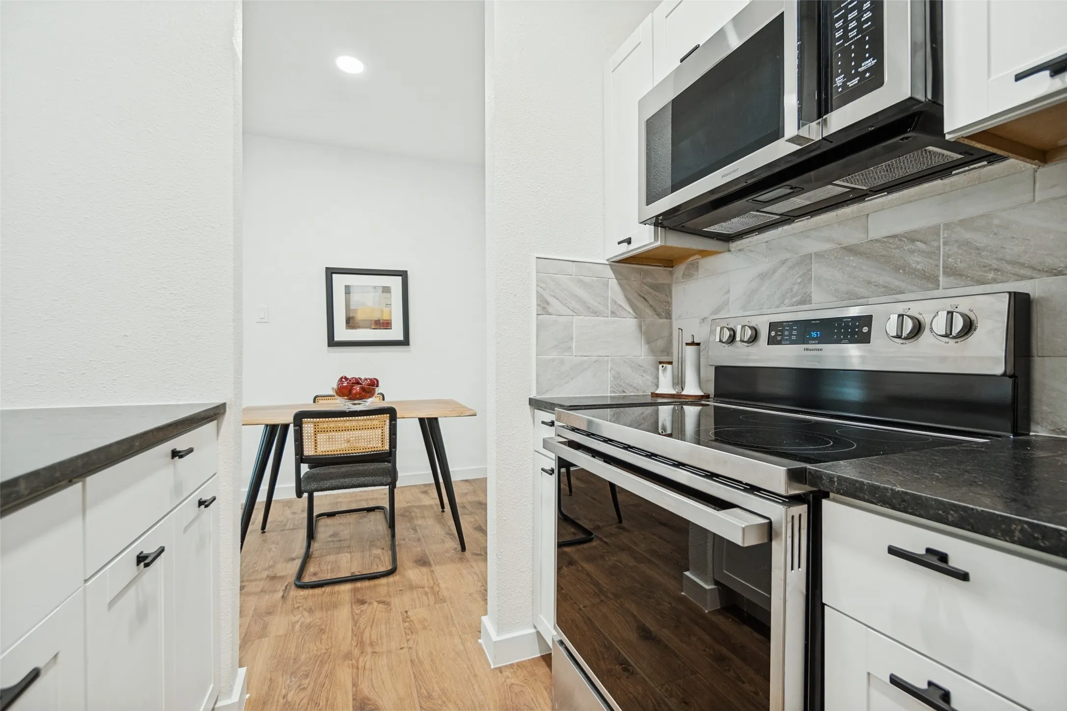 Sleek kitchen featuring stainless steel appliances, dark countertops, white cabinetry, a tiled backsplash, and wood-finish flooring