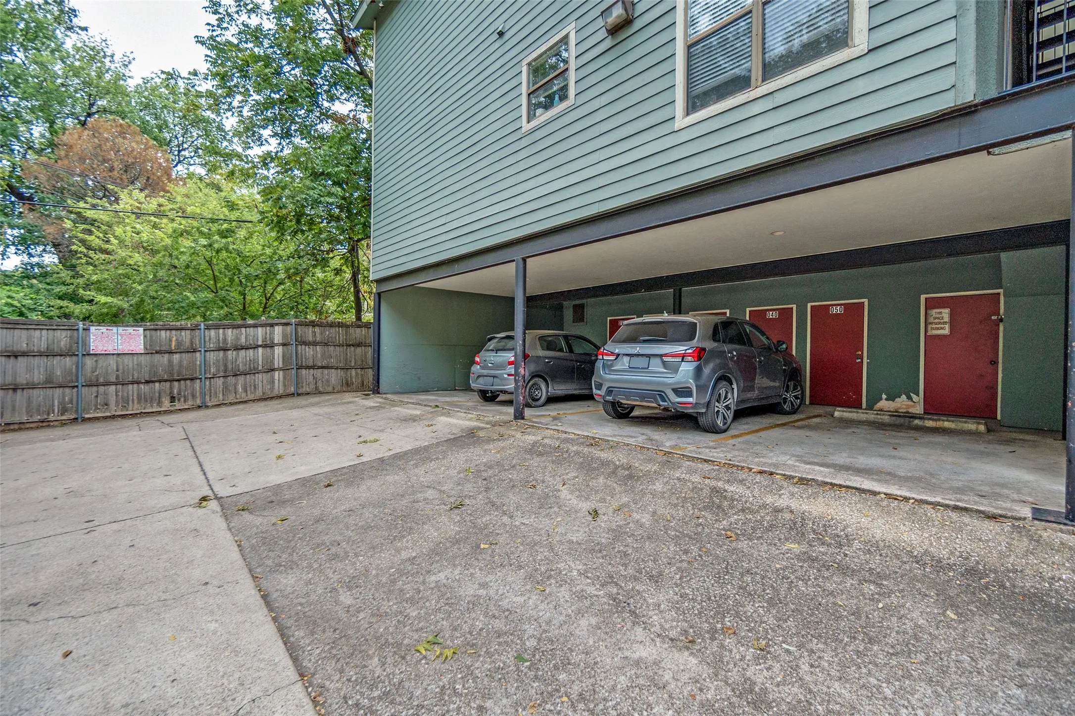 Covered parking area with concrete flooring, wood privacy fence, and multiple storage units