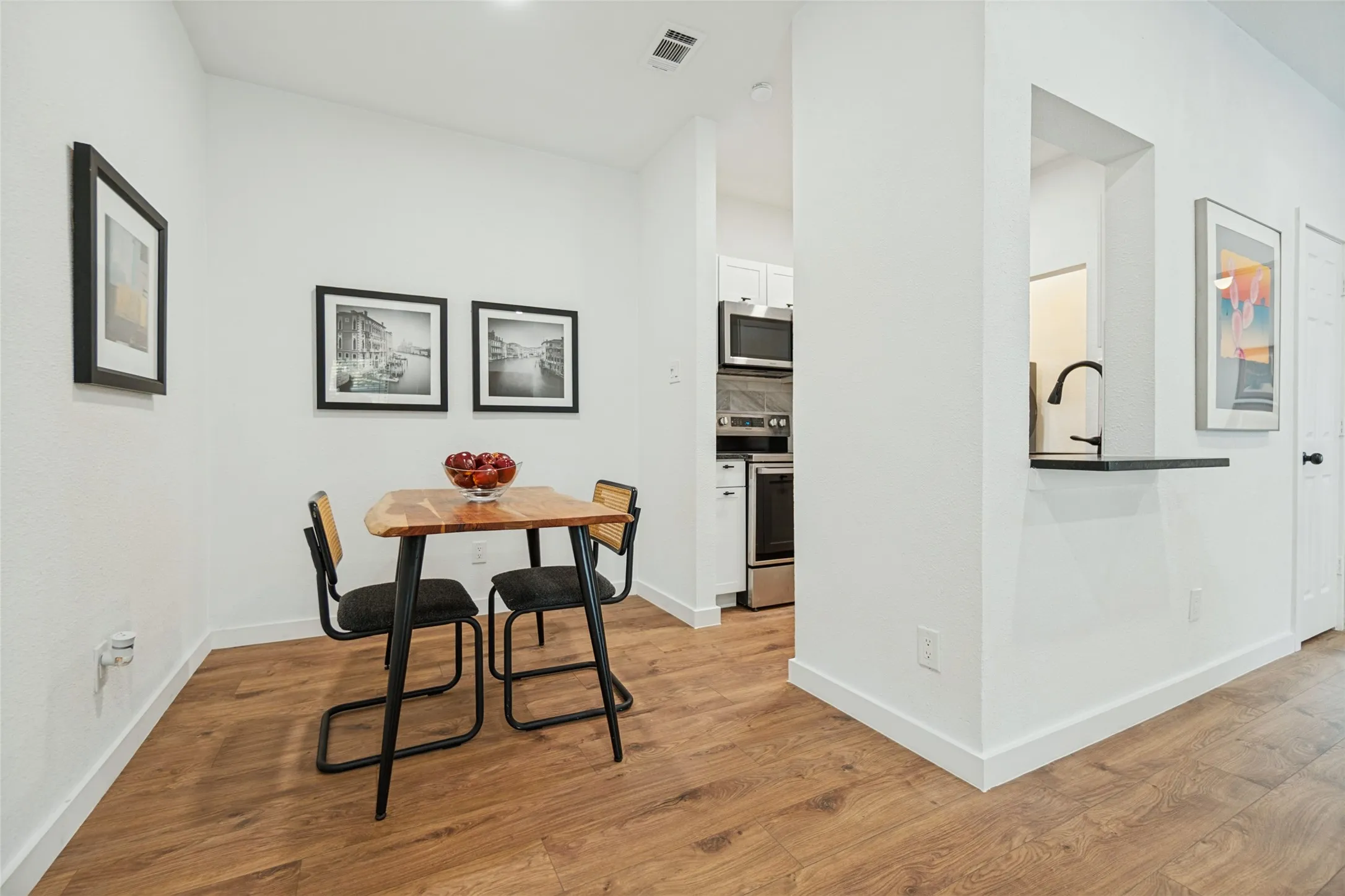 Wood-finish flooring throughout, white walls, and a pass-through window with a dark countertop