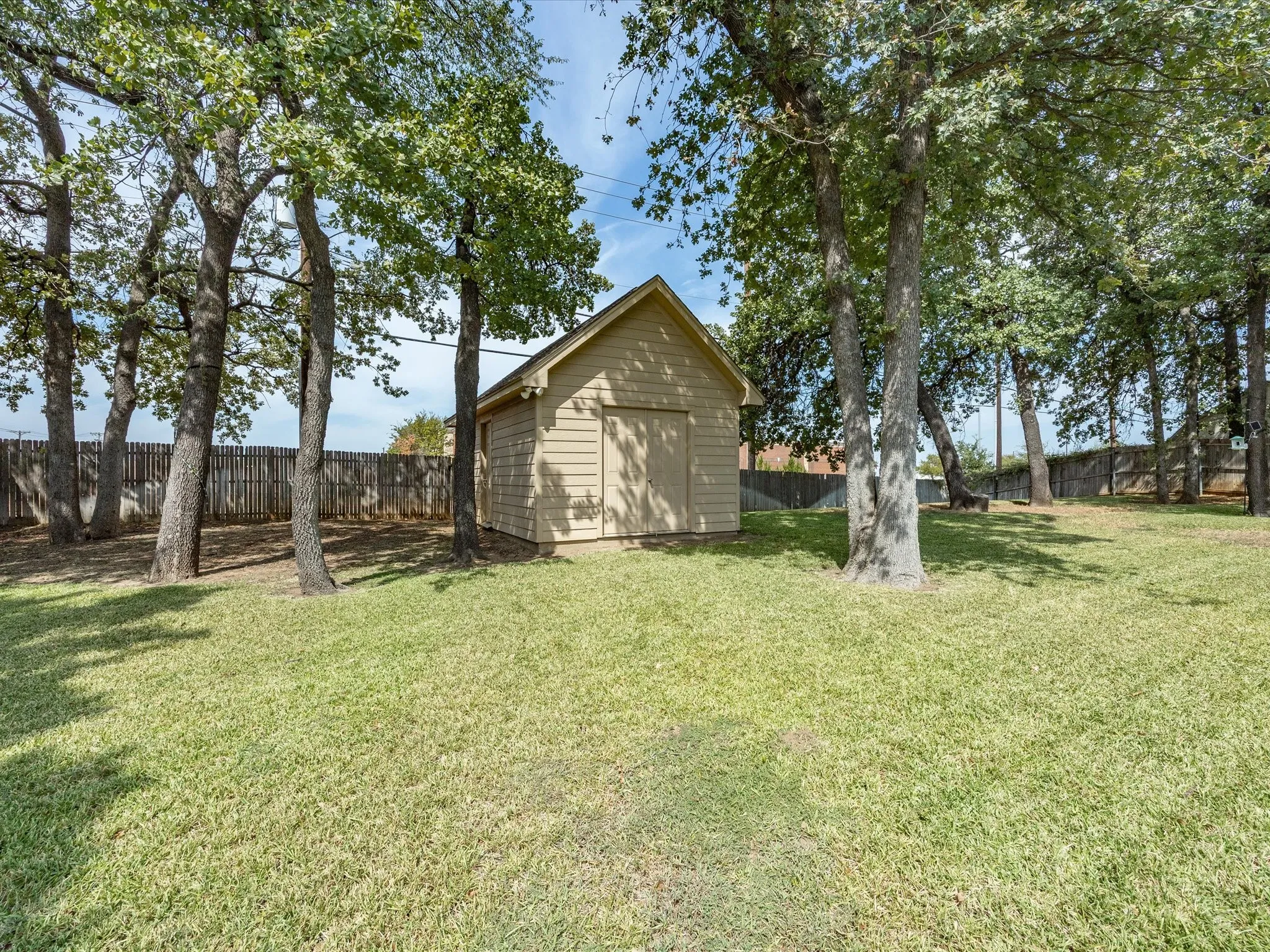 Expansive backyard featuring a manicured lawn, a storage shed with siding, and mature trees