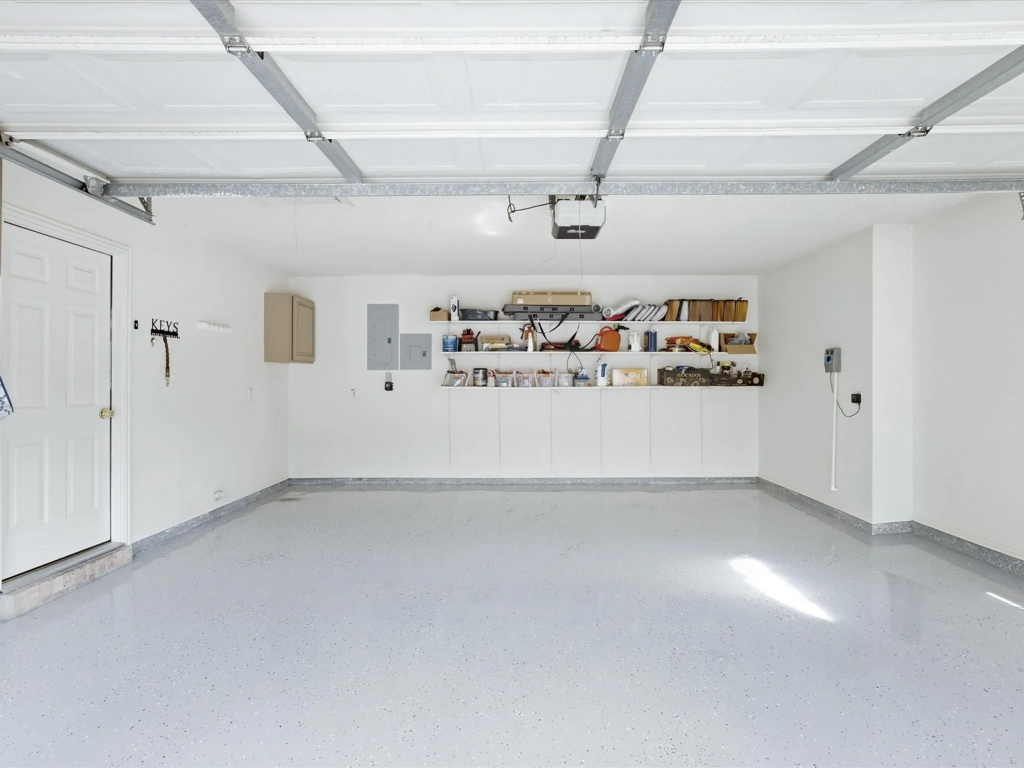 Garage with epoxy flooring, white walls, built-in lower cabinetry, and open shelving