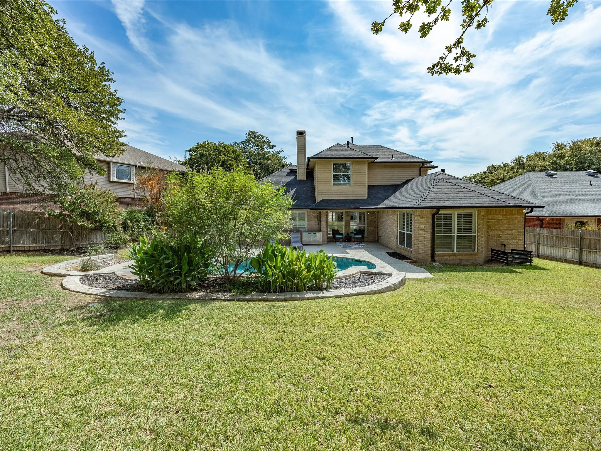 Expansive green lawn with a swimming pool, stone-edged landscaping, and a brick and siding exterior
