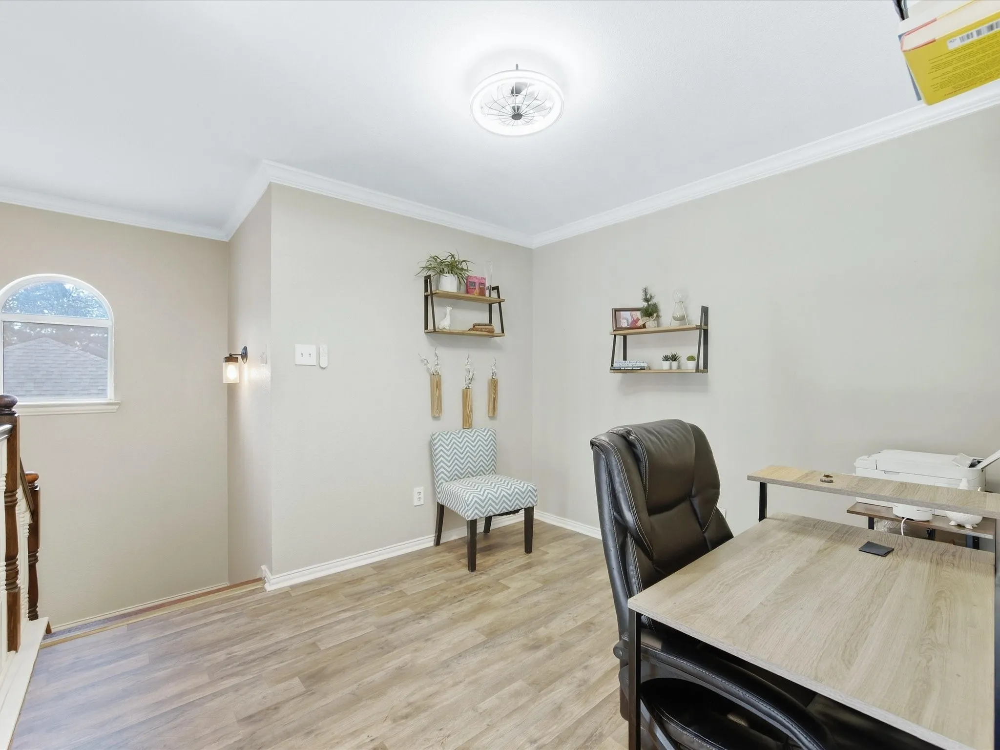 Wood-finish flooring, crown molding, arched window, wall sconce lighting, and a ceiling-mounted light fixture