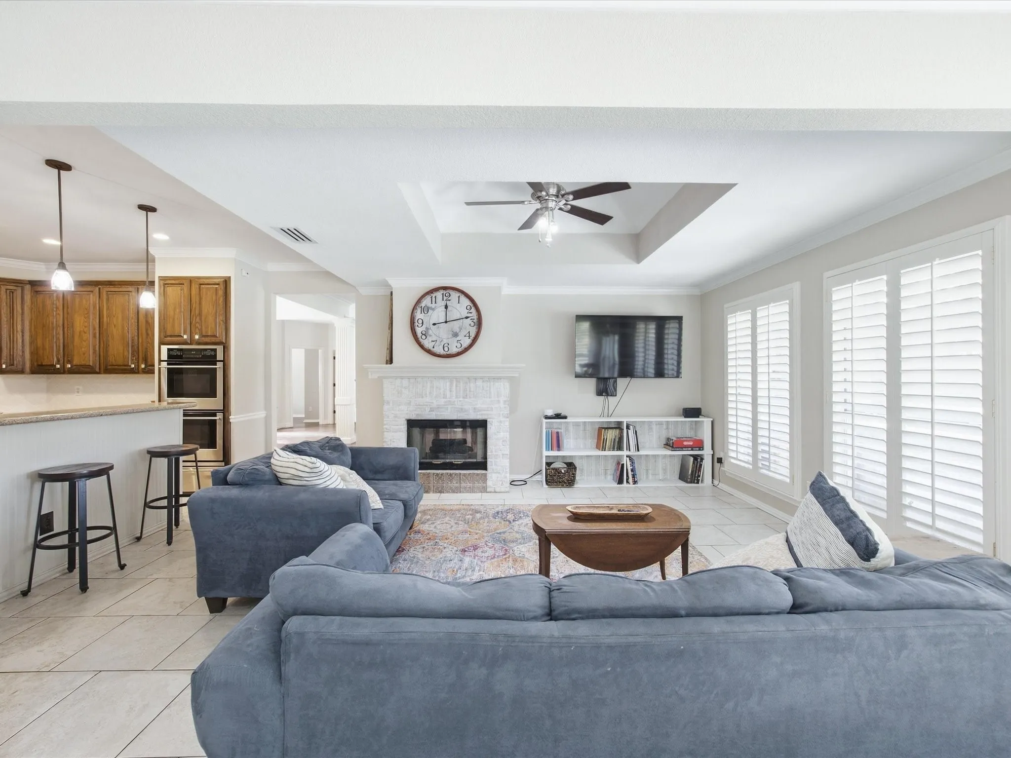 Open-concept living area featuring a curved sectional sofa arrangement, tile flooring, and abundant natural light from multiple glass doors with plantation shutters