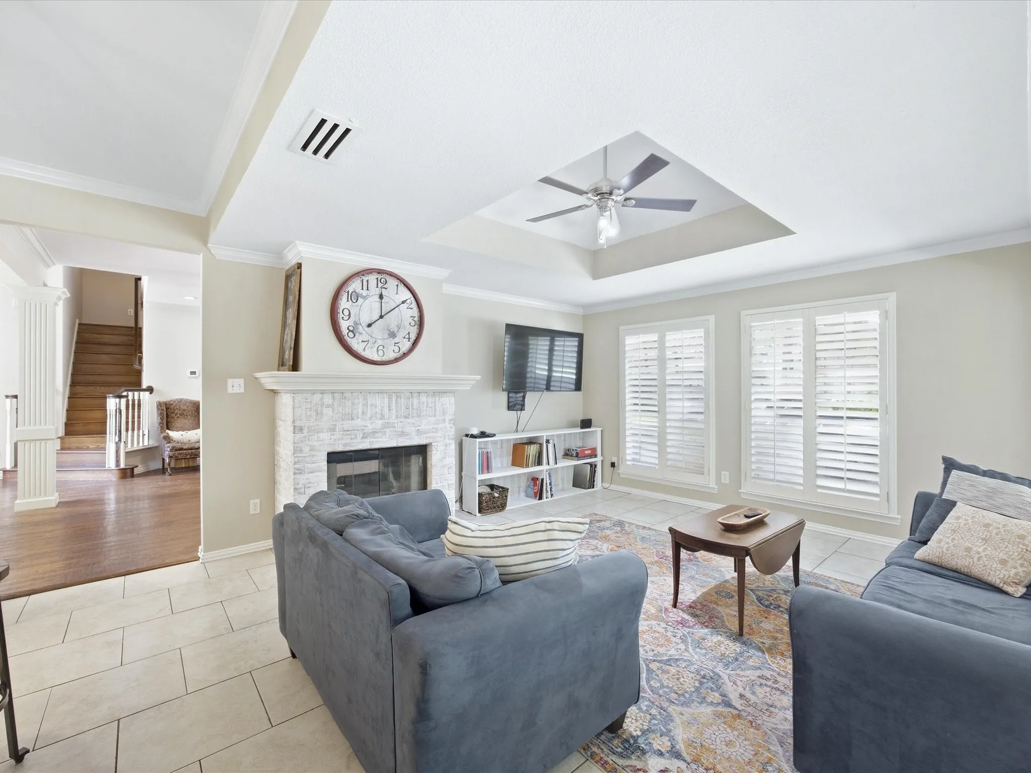 Living area featuring a textured tile floor, white fireplace surround, and a tray ceiling with a ceiling fan