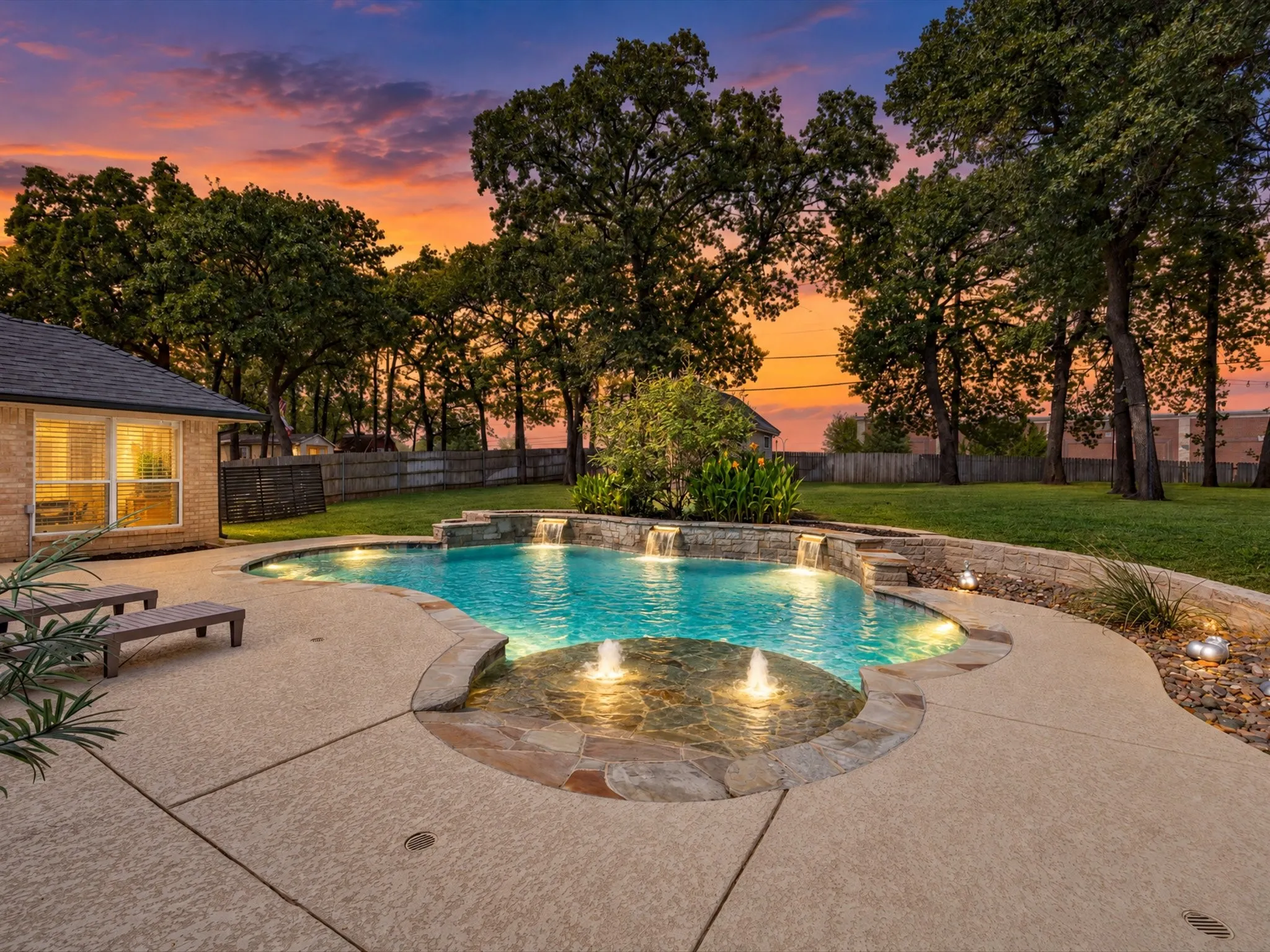 Resort-style pool with integrated spa and water features, surrounded by extensive concrete decking and mature trees