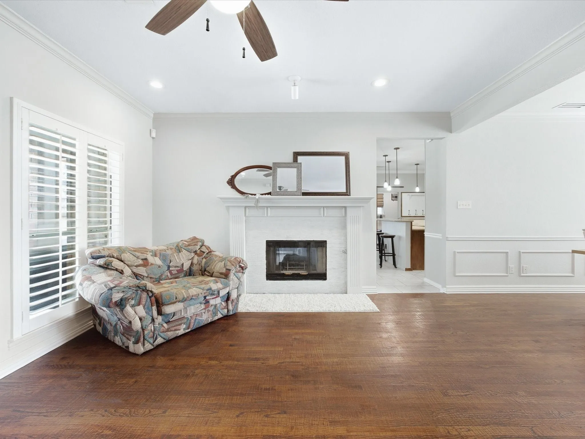 Wood-finish flooring, white fireplace with a dark firebox, white window shutters, crown molding, and recessed lighting