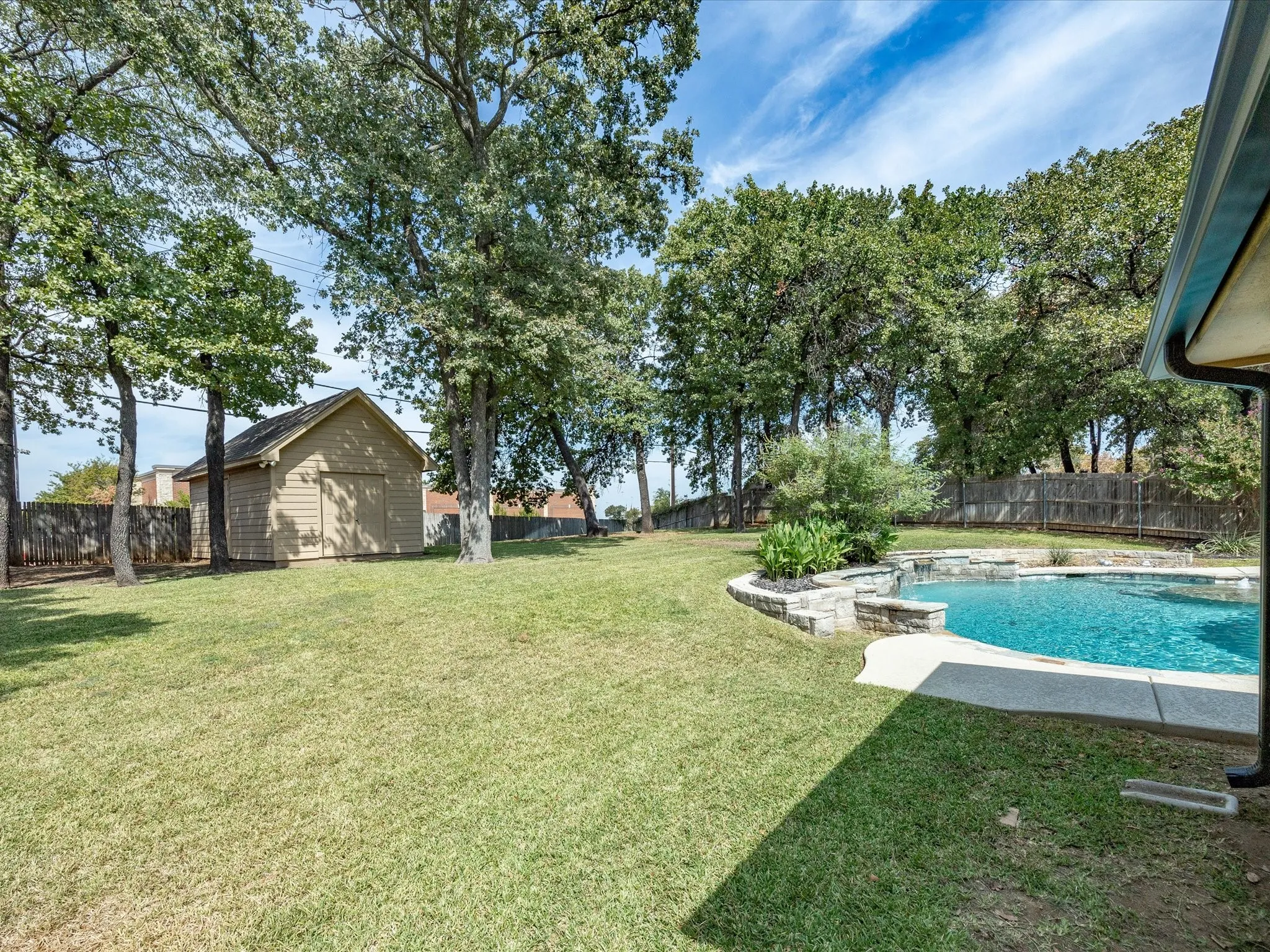 Expansive yard featuring a swimming pool with stone surround, a dedicated storage shed, and mature trees