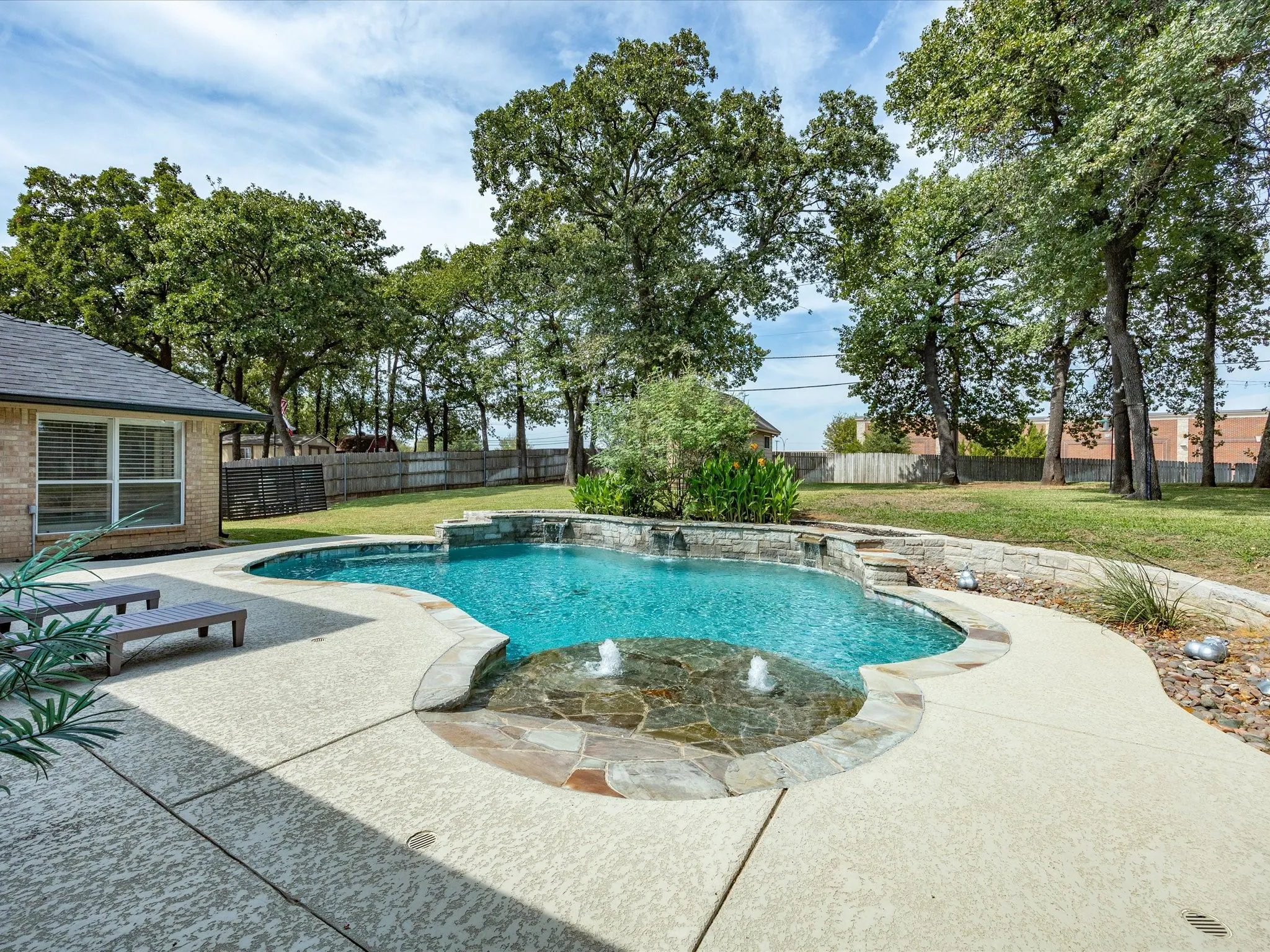 Landscaped backyard featuring a custom swimming pool with stone accents, a built-in spa with water features, a stone retaining wall, and a spacious concrete patio