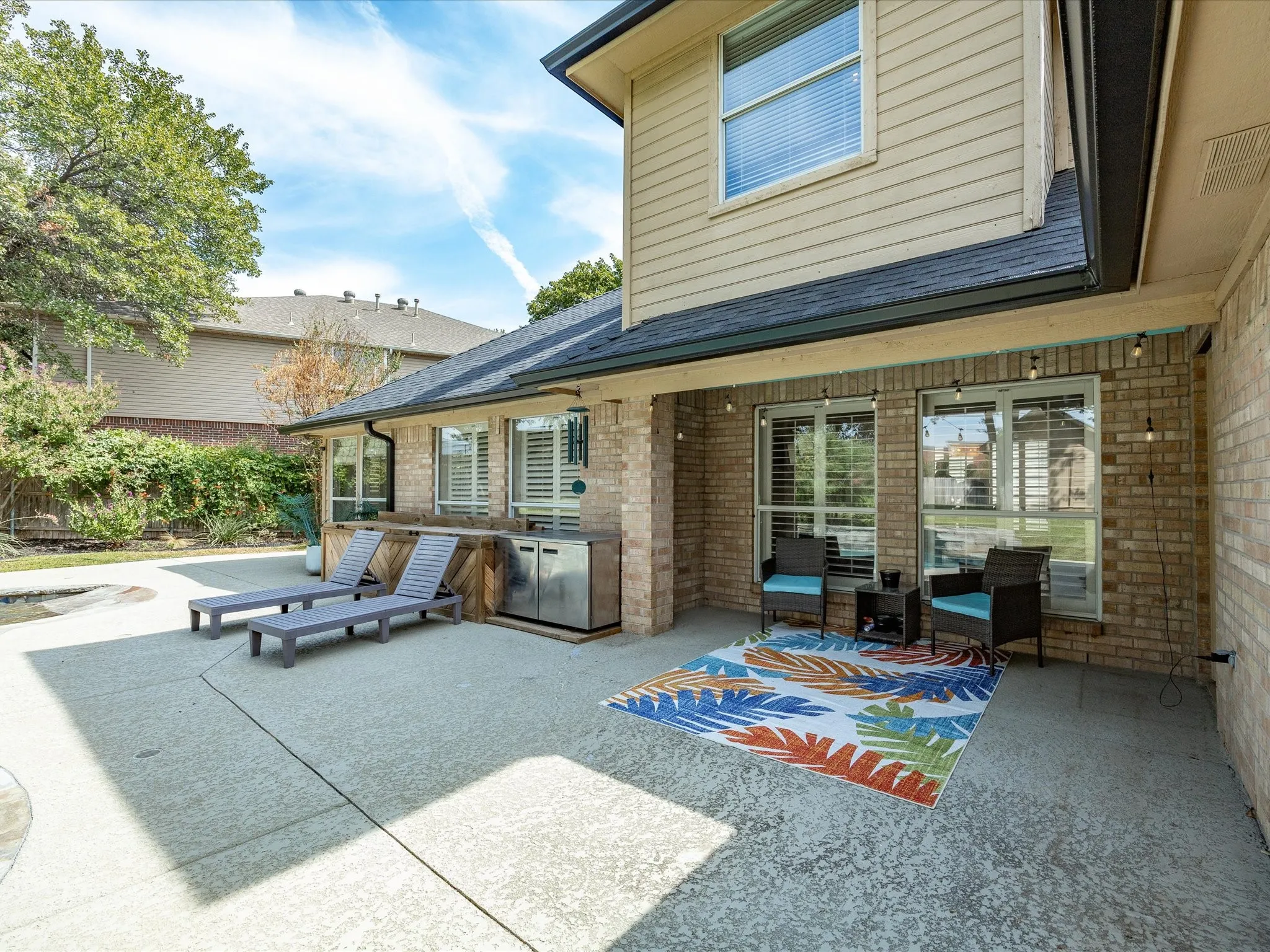 Expansive concrete patio with a covered outdoor entertaining area, built-in outdoor kitchen with stainless steel appliances, and a pool deck