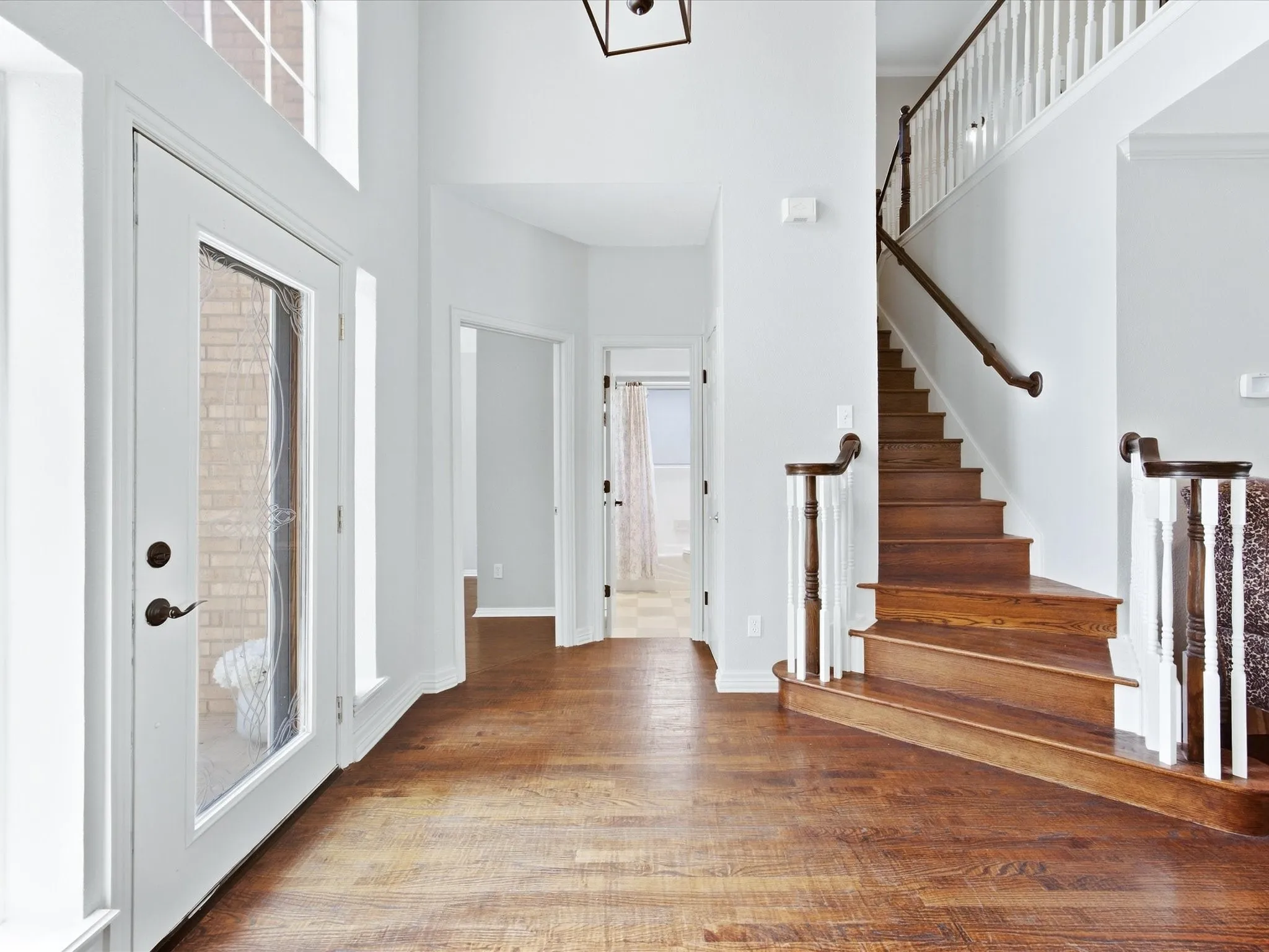 Spacious entryway featuring wood-finish flooring, a grand staircase with wood treads and white balusters, and a transom window above the entry door