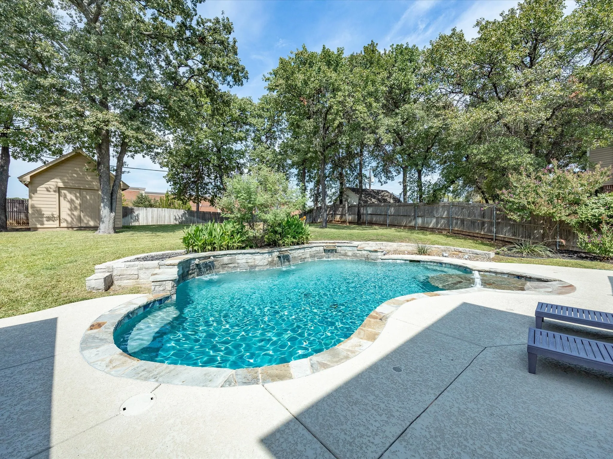 Freeform swimming pool with stone coping, integrated spa, and concrete decking