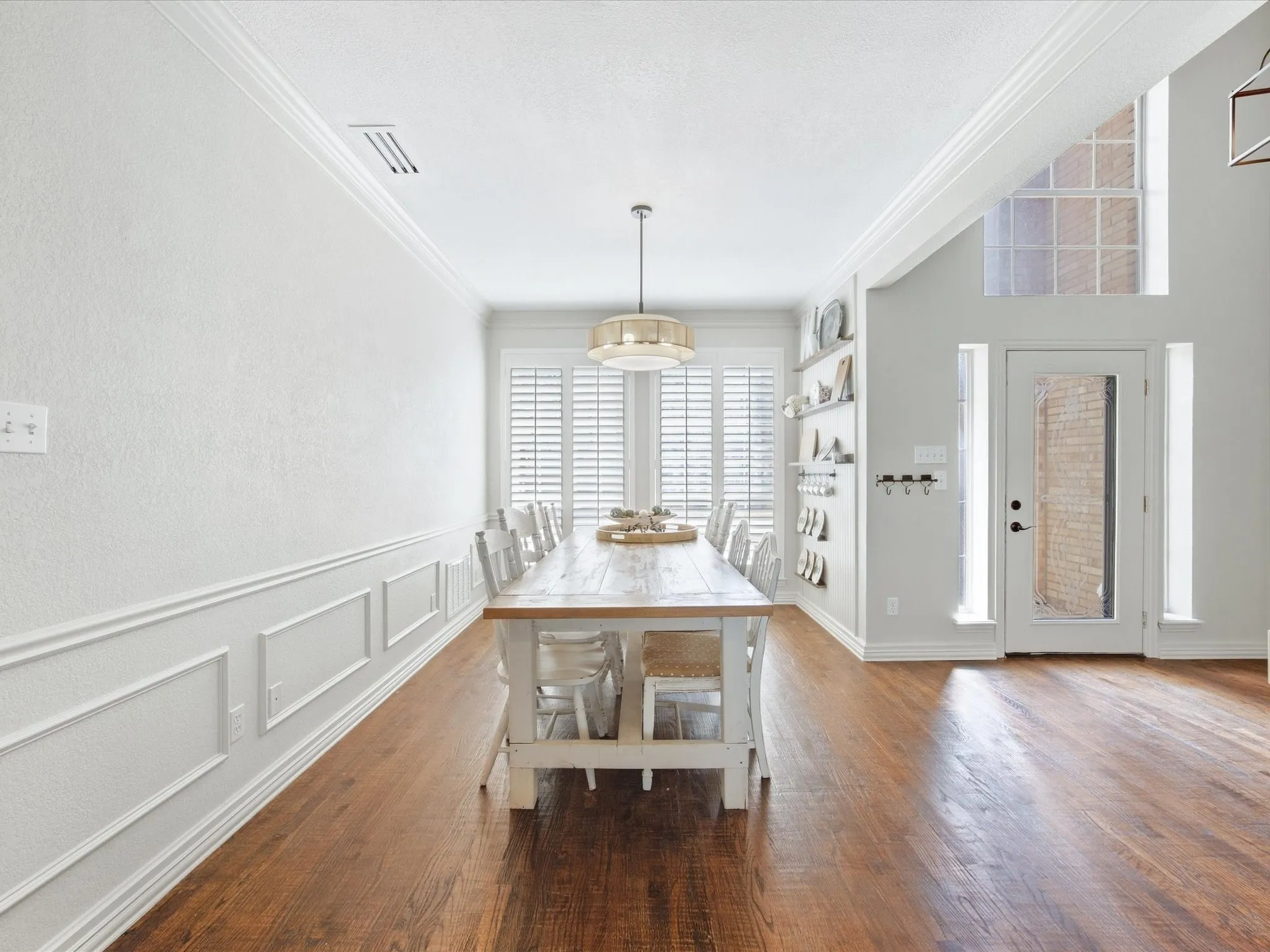 Wood-finish flooring, crown molding, wainscoting, plantation shutters, and a transom window