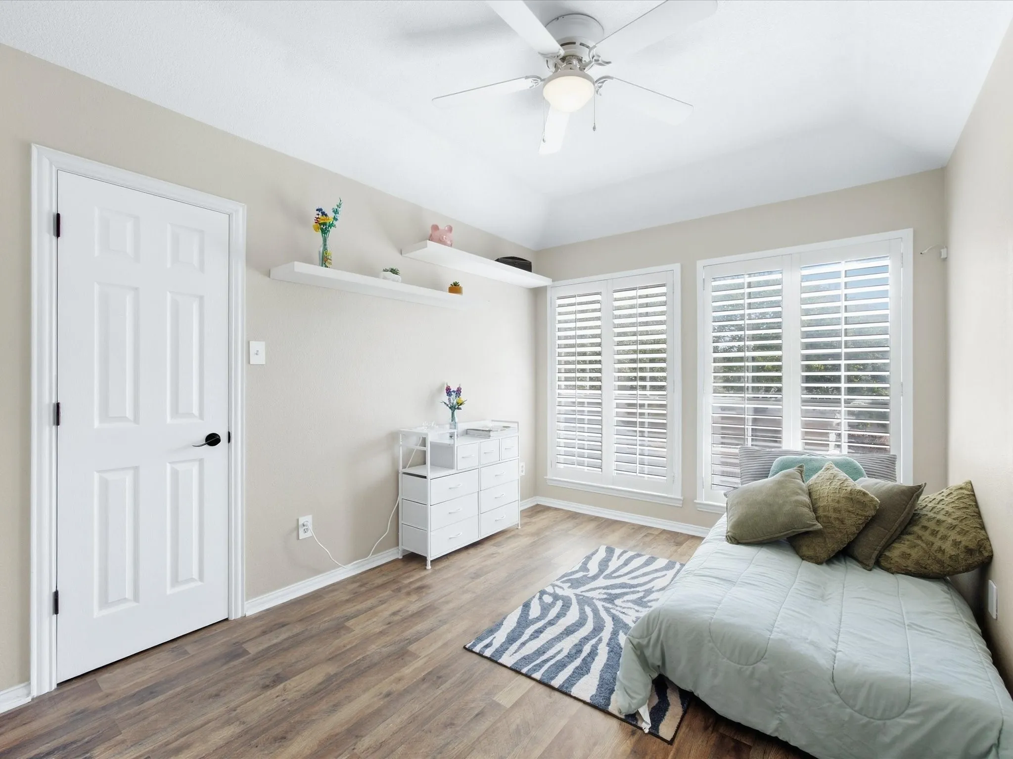 Vaulted ceiling, wood-finish flooring, ceiling fan, multiple windows with plantation shutters, and built-in shelving