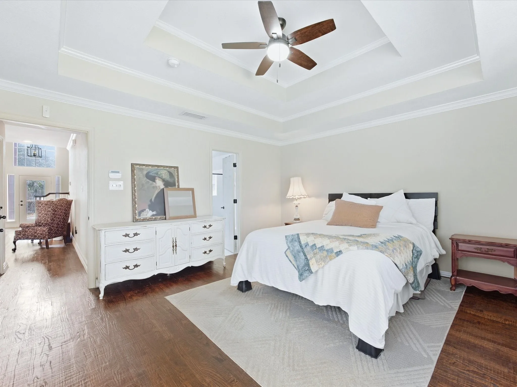 Tray ceiling with crown molding and a ceiling fan, wood-finish flooring, and light-colored walls