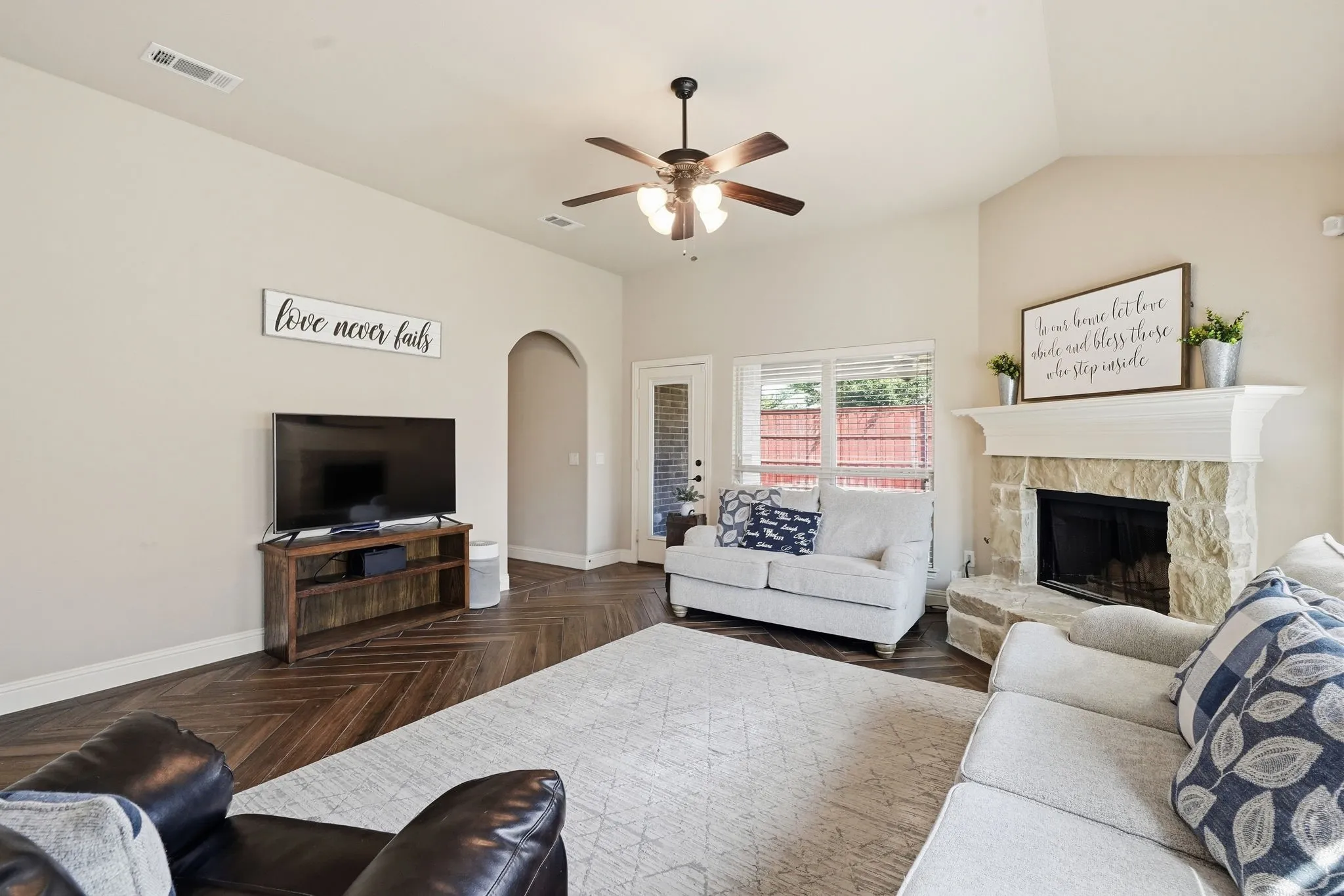 Vaulted ceiling, wood-finish flooring, stone-faced fireplace with mantel, ceiling fan, and arched doorway
