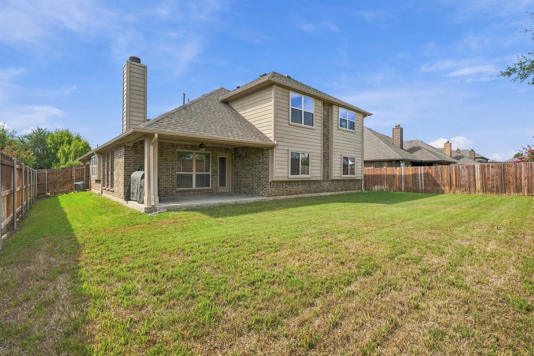 Expansive backyard with a full privacy fence, covered concrete patio, and brick exterior details