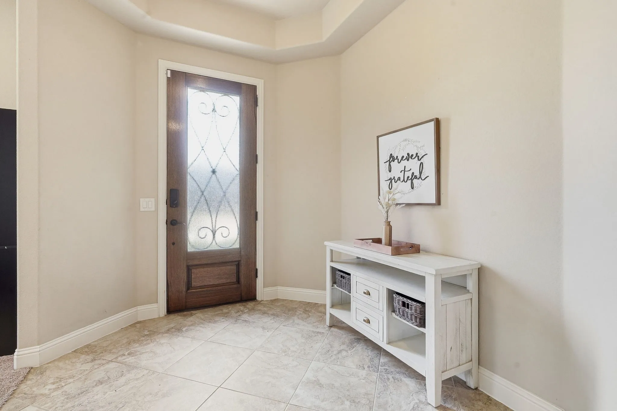 Impressive entry featuring a rich walnut-stained, glass-paneled front door, warm neutrals & tray ceiling