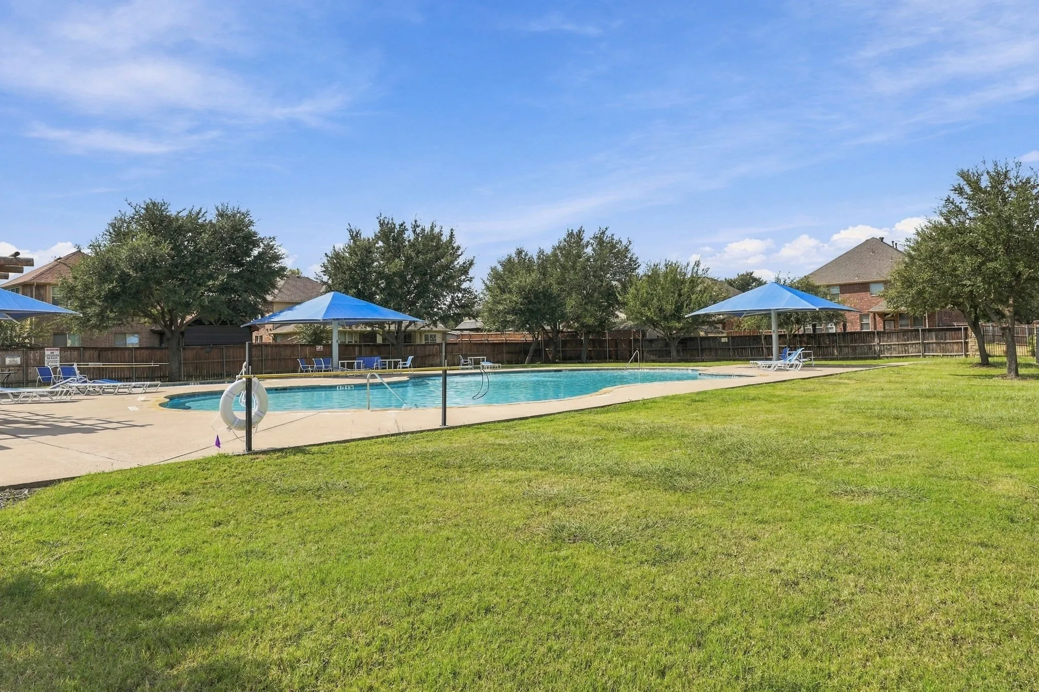 Expansive grassy area with a swimming pool, concrete pool deck, and perimeter fencing