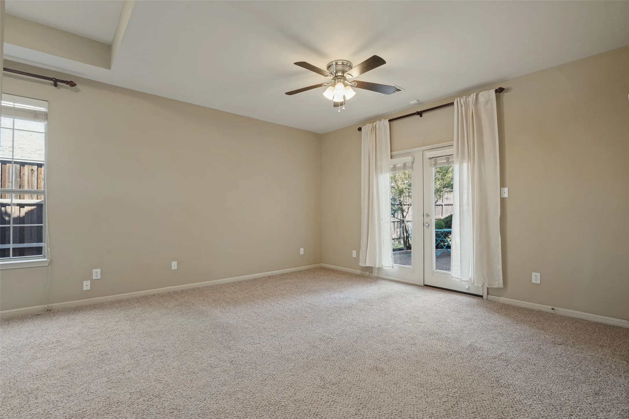 The primary suite features tray ceiling with recessed lighting, ceiling fan with integrated lighting, glass French doors leading to the back patio, and neutral carpeting
