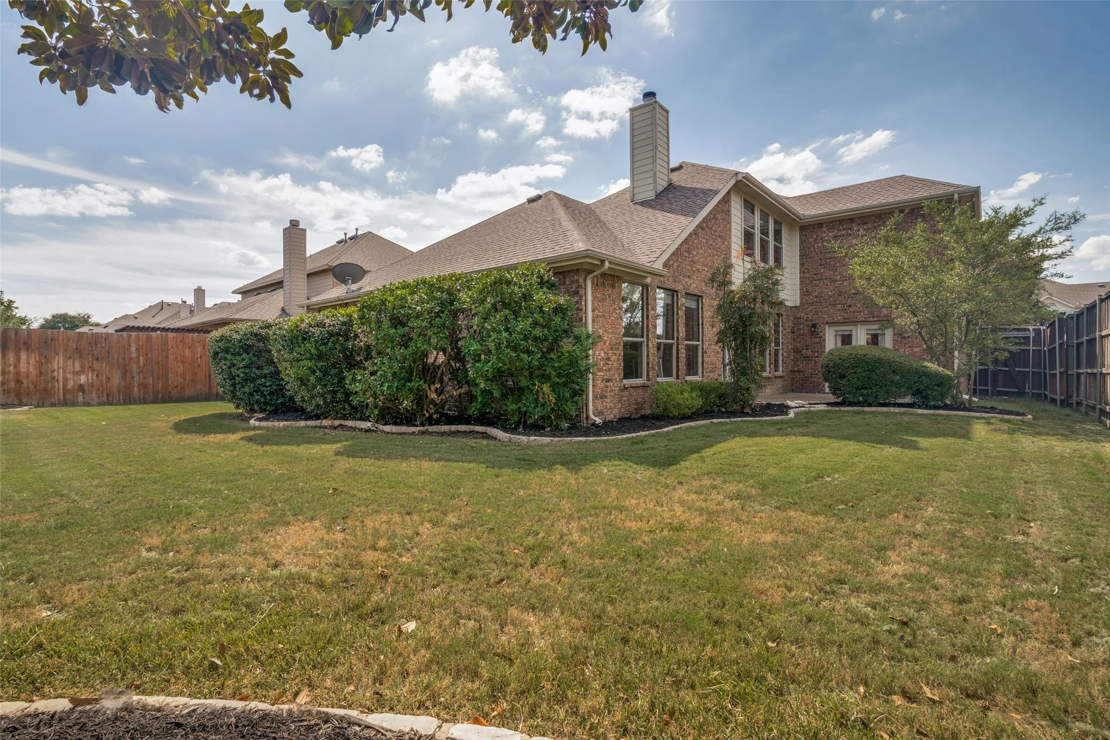 Expansive backyard featuring a brick exterior, multiple large windows, mature shrubs, and a wood privacy fence plenty of room for a future pool or orher use