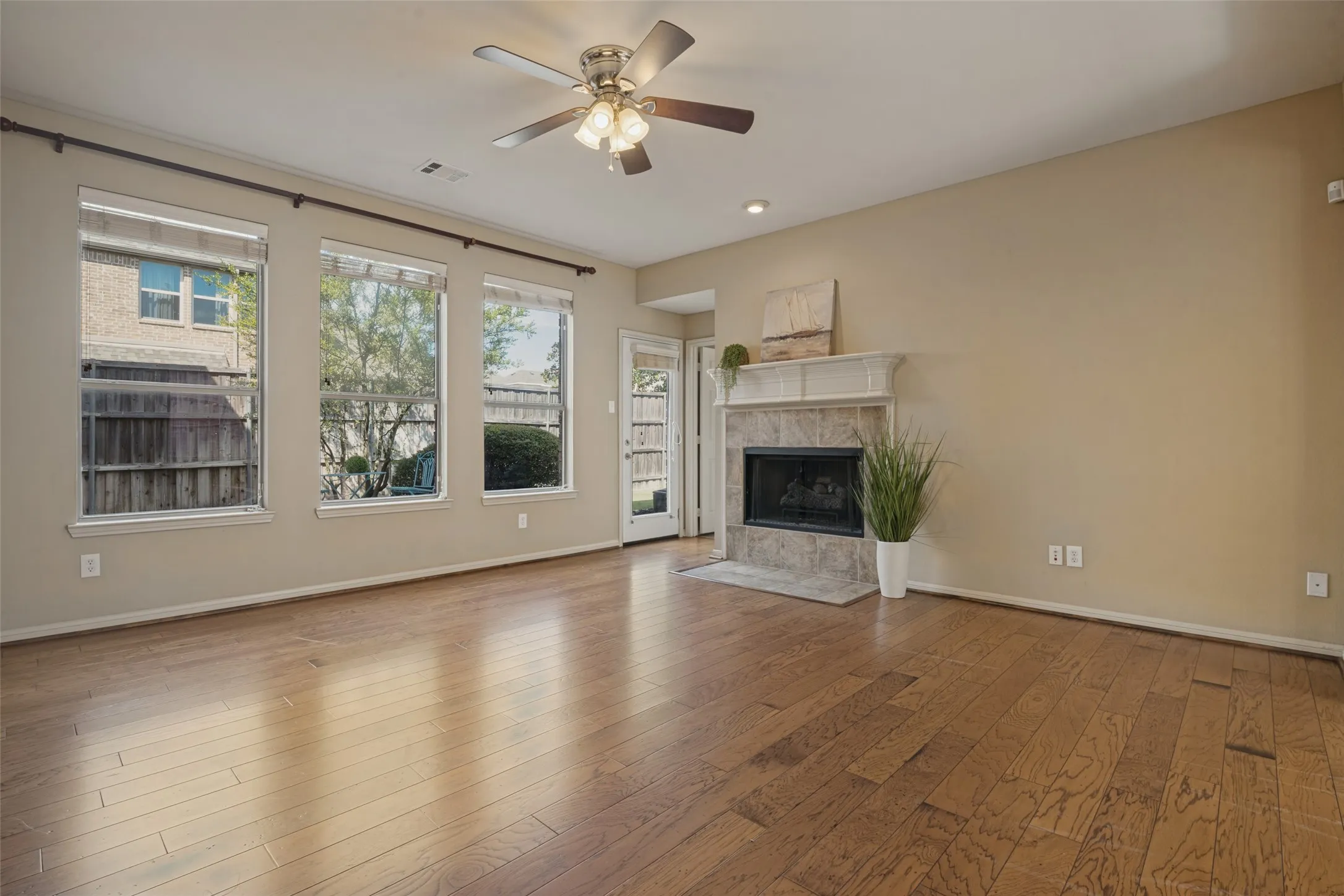 The living room boasts Hardwood-finish flooring throughout, ceiling fan with integrated lighting, multiple windows, stone-surround fireplace with mantel, and a door with glass panels