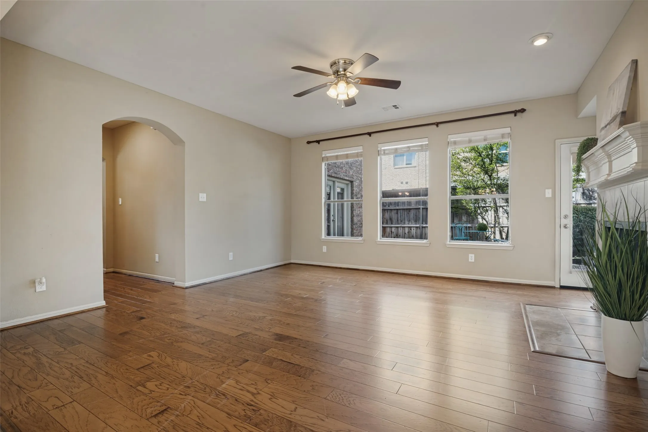 The living room hasHardwood flooring, arched doorway, three windows, ceiling fan with integrated lighting, and a fireplace with a mantel