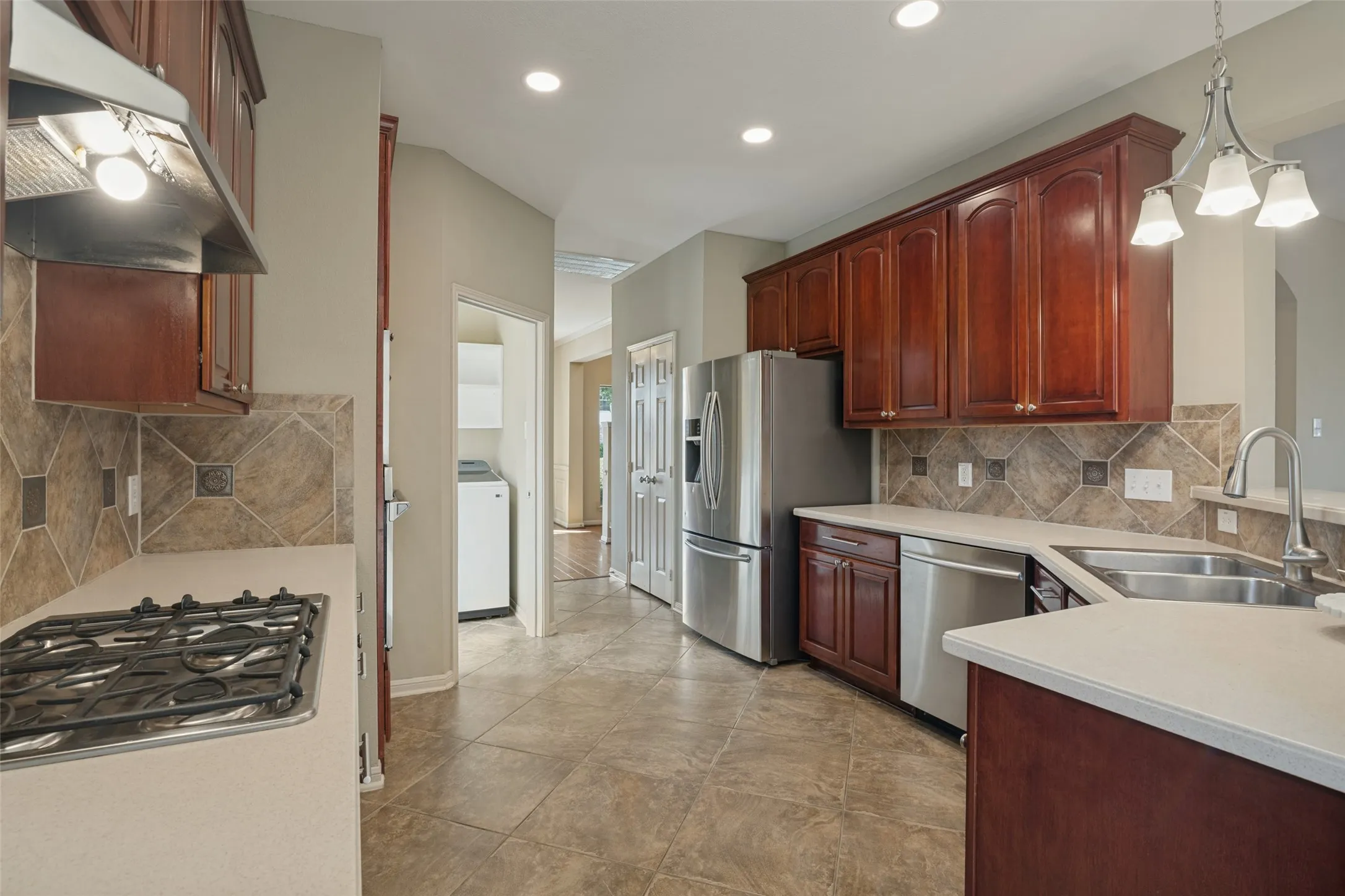 Kitchen featuring extensive wood cabinetry, stainless steel appliances, tiled flooring, and a coordinating tiled backsplash