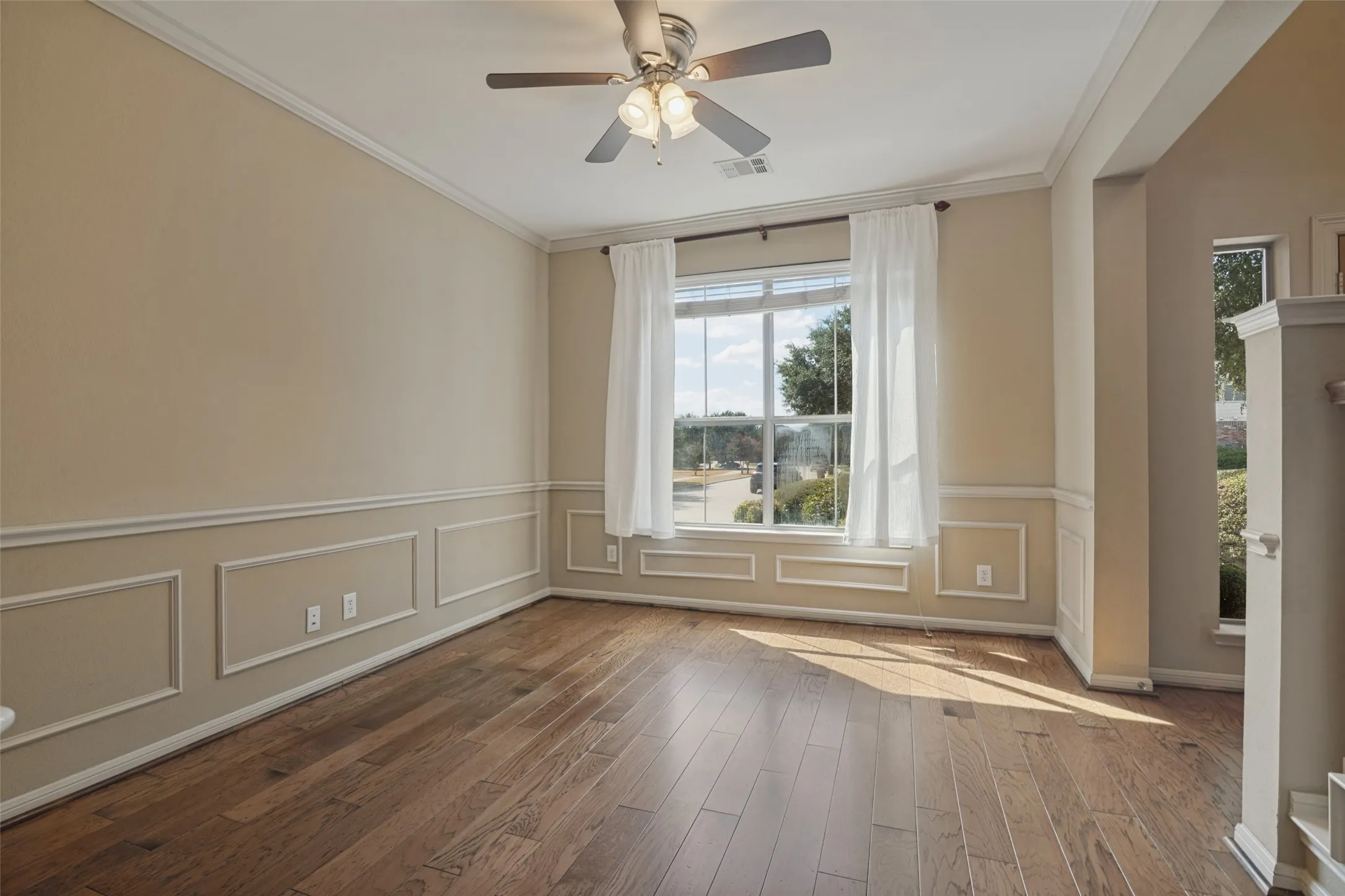 The formal dining room features Hardwood flooring, crown molding, chair rail molding, ceiling fan, and large window