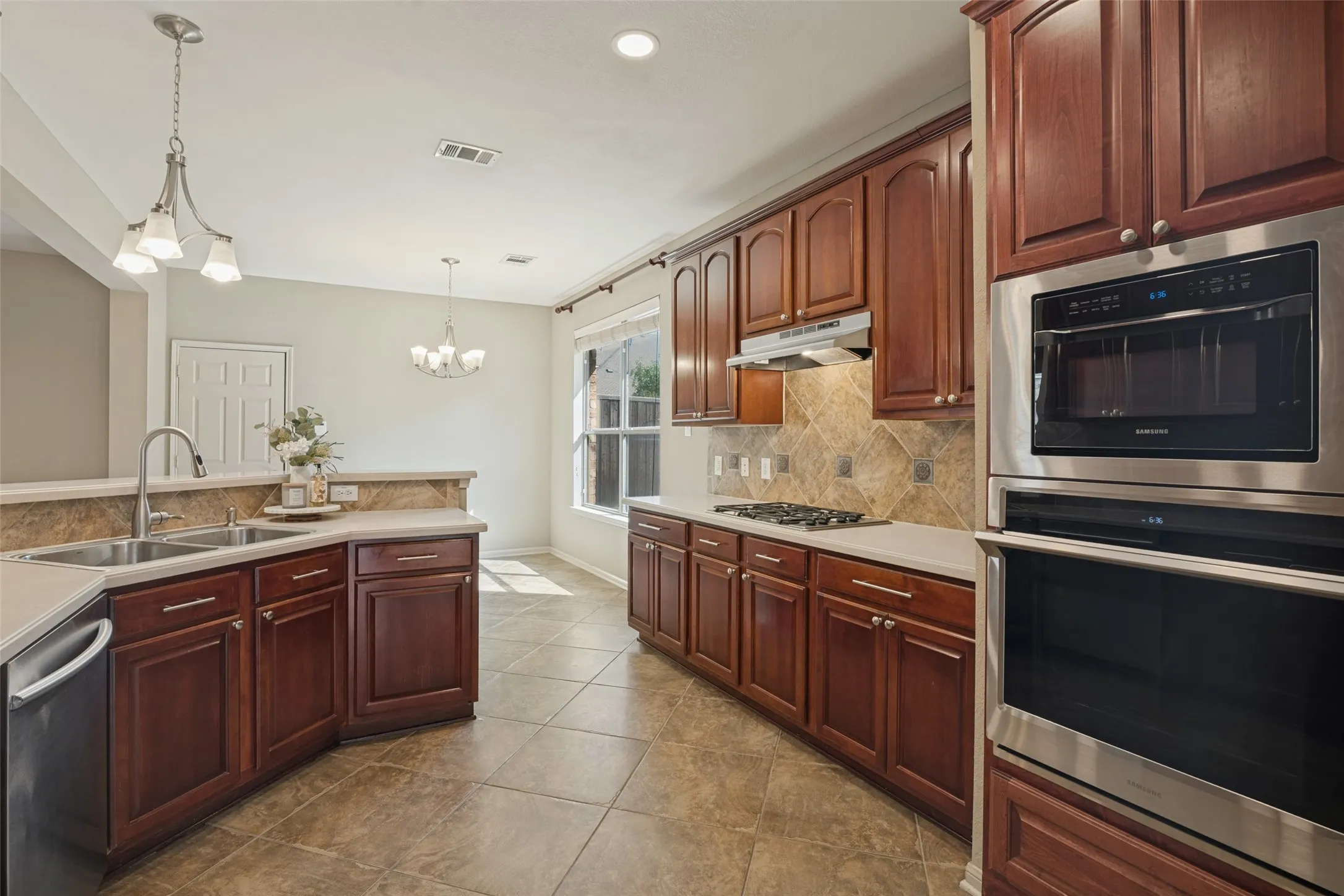 Kitchen featuring dark wood cabinetry, stainless steel appliances, light countertops, and tile flooring, microwave and oven, gas cook top