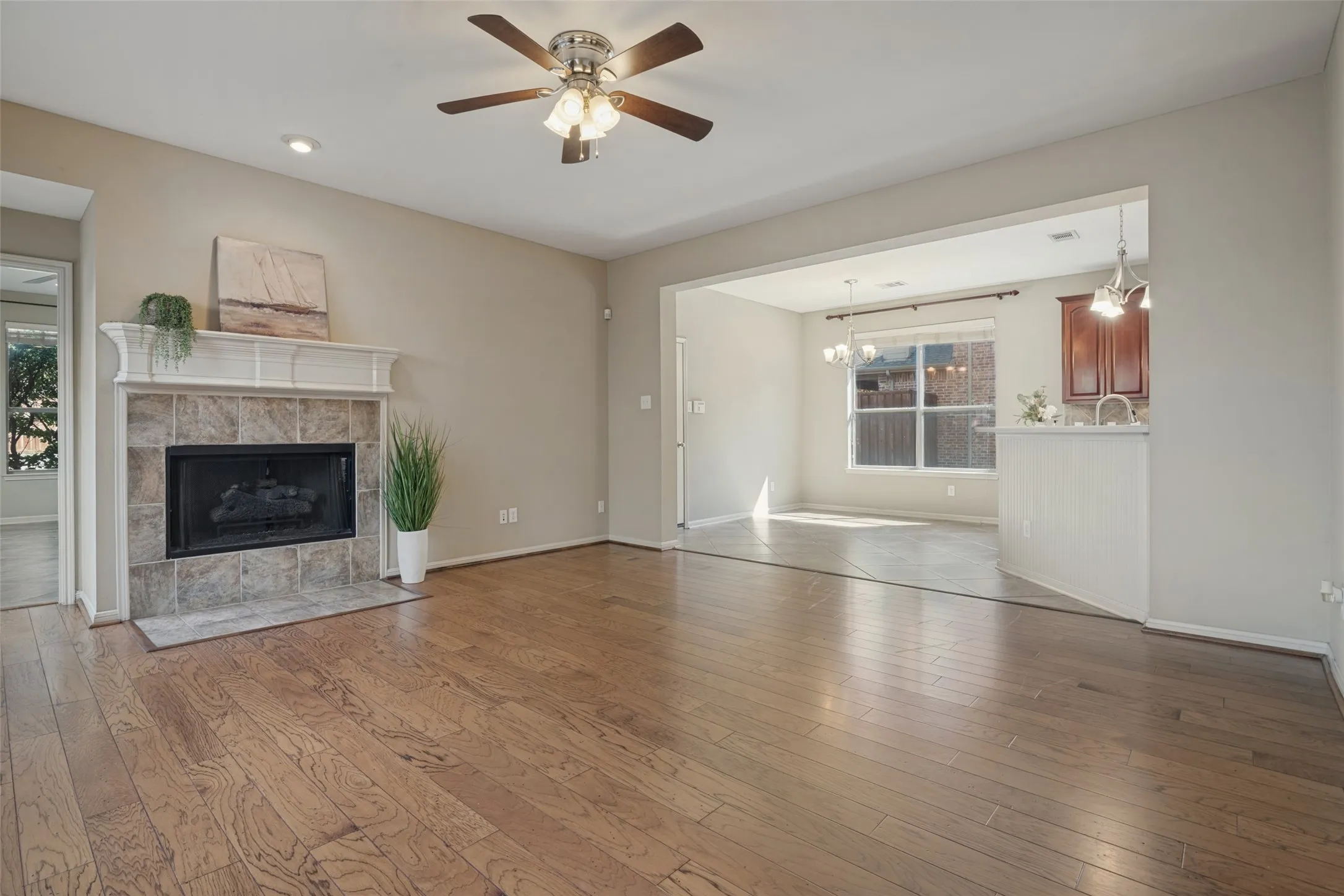 Wood-finish flooring throughout, fireplace with a tiled surround and mantel, recessed lighting, ceiling fan with light fixture, and an archway leading to the sunroom