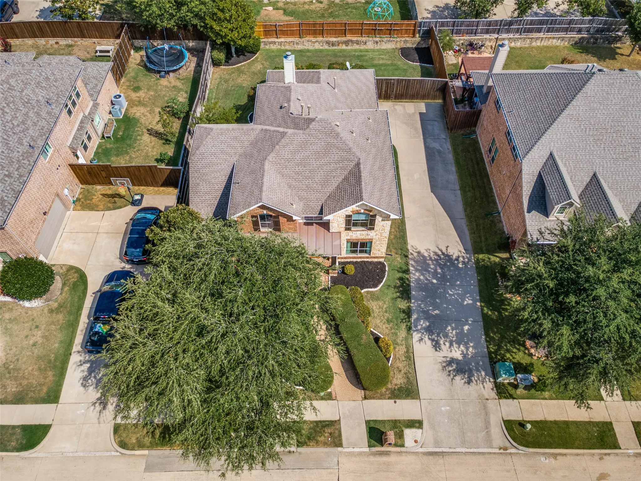 Stone and brick exterior with a multi-level roofline, concrete driveway, front yard landscaping, and a fenced backyard