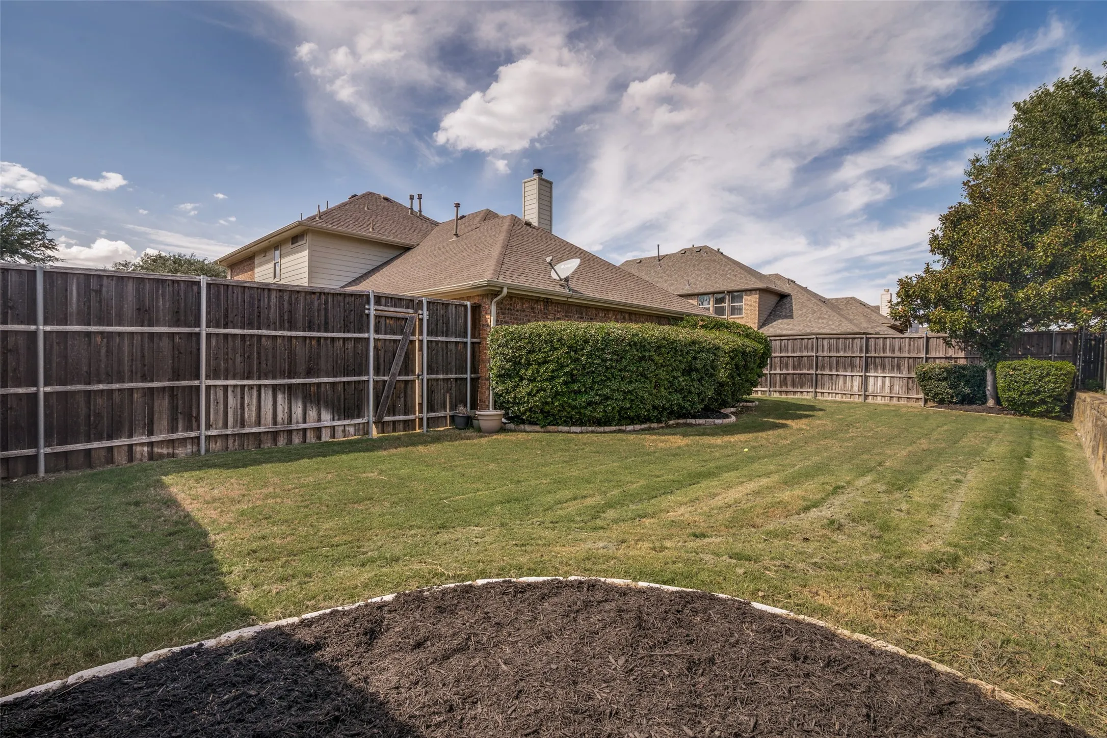 Expansive backyard featuring a manicured lawn, established privacy fencing, and mature shrubbery