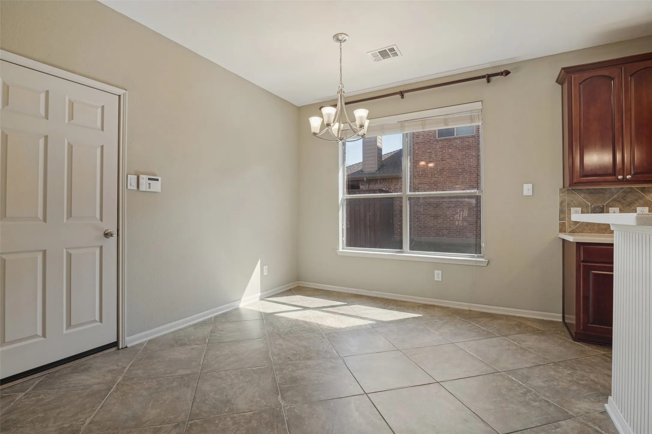 The breakfast nook or eat in kitchen has Tile flooring, pendant light fixture, window with blinds, dark wood-finish cabinetry, and tiled backsplash