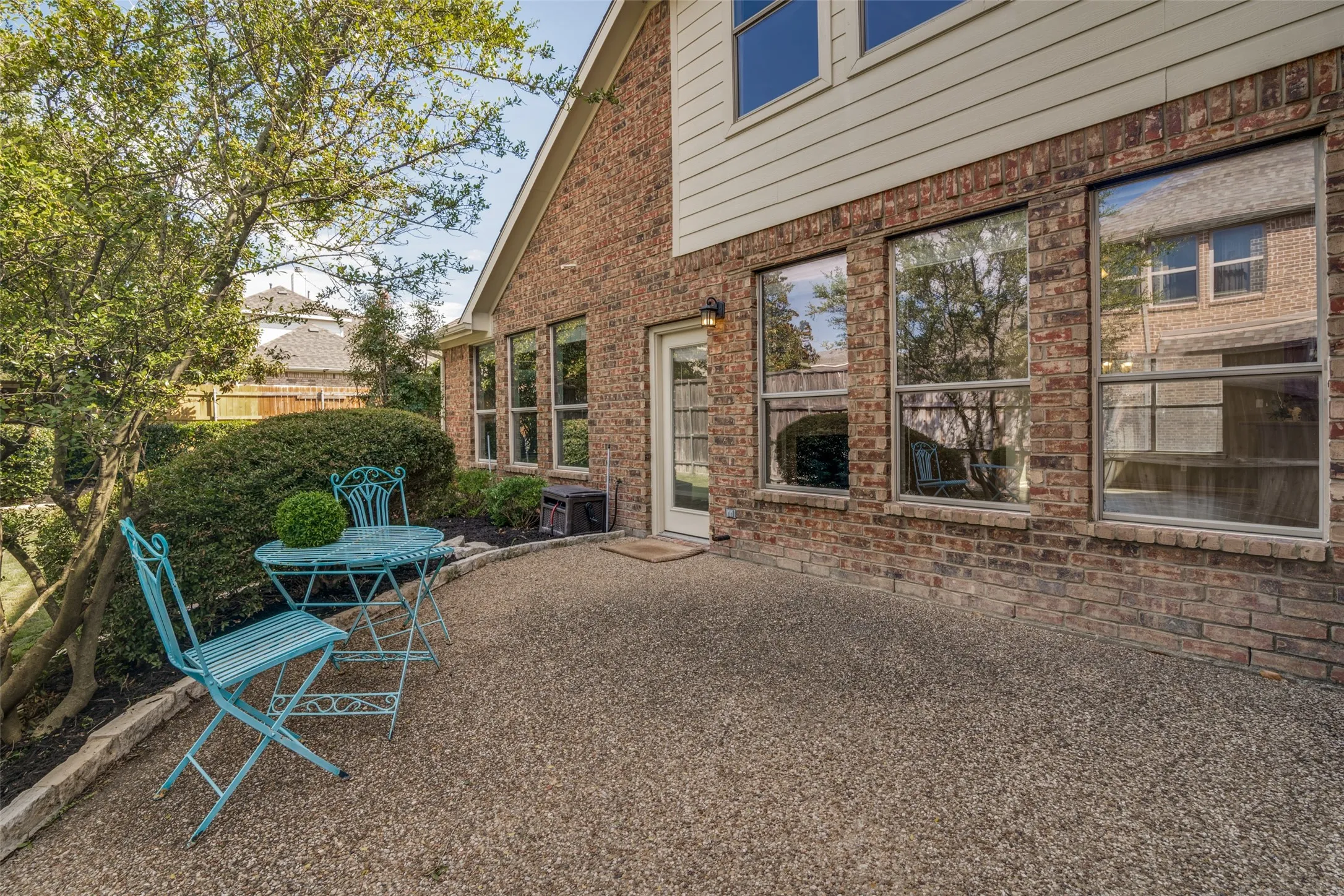 Back yard patio has a gas line for a future geill, brick exterior featuring multiple large windows, a single glass-paneled door, and a textured concrete patio