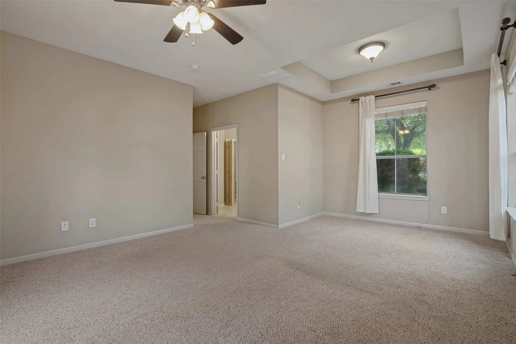 the primary suite has tray ceiling, recessed lighting, ceiling fan, and carpeted flooring, extra sitting area, ensuite bath and walk in closet