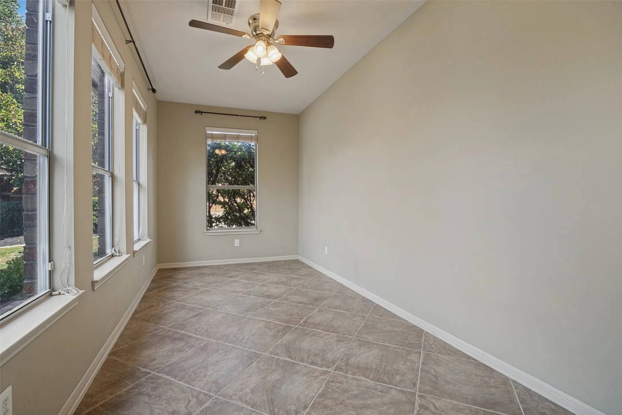 Neutral-toned ceramic tile flooring, multiple double-hung windows, and a ceiling fan with light fixture, the sunroom could be the perfect office, art studio, toy or pet room