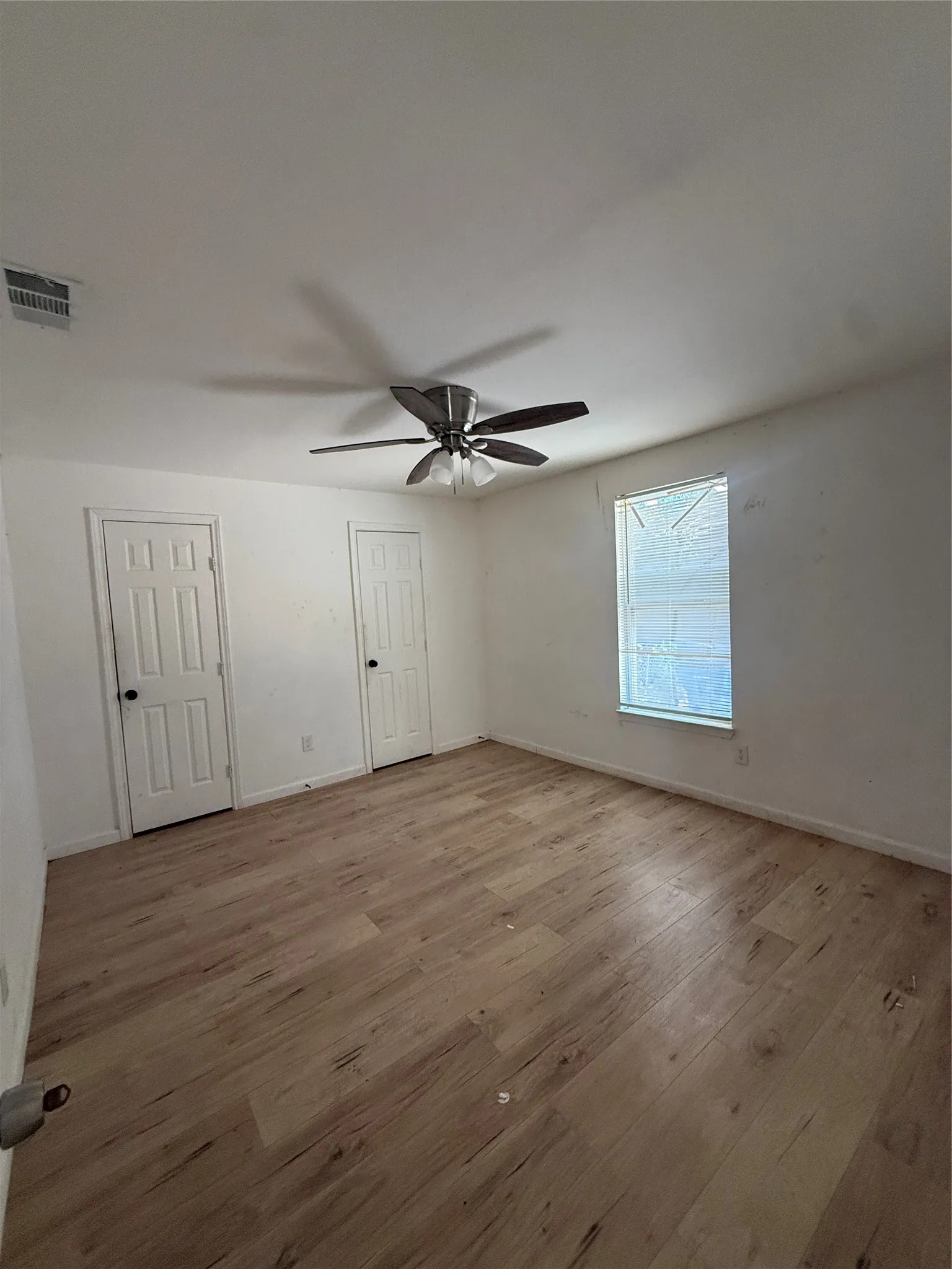 Wood-finish flooring throughout, two panel doors with dark hardware, and a ceiling fan with integrated lighting