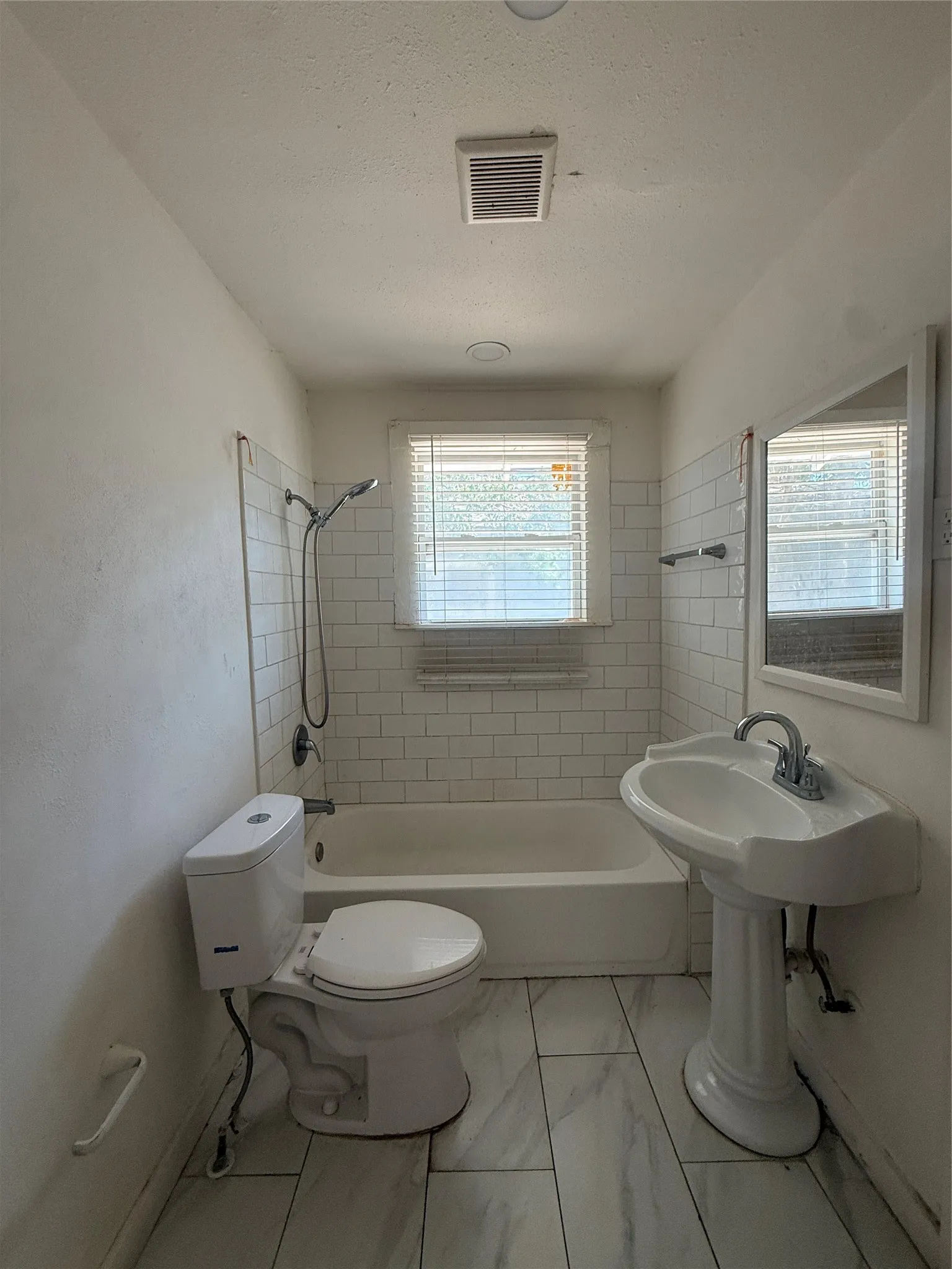 Pedestal sink with chrome faucet, subway tile bath surround, white bathtub, porcelain toilet, and light-toned tile flooring