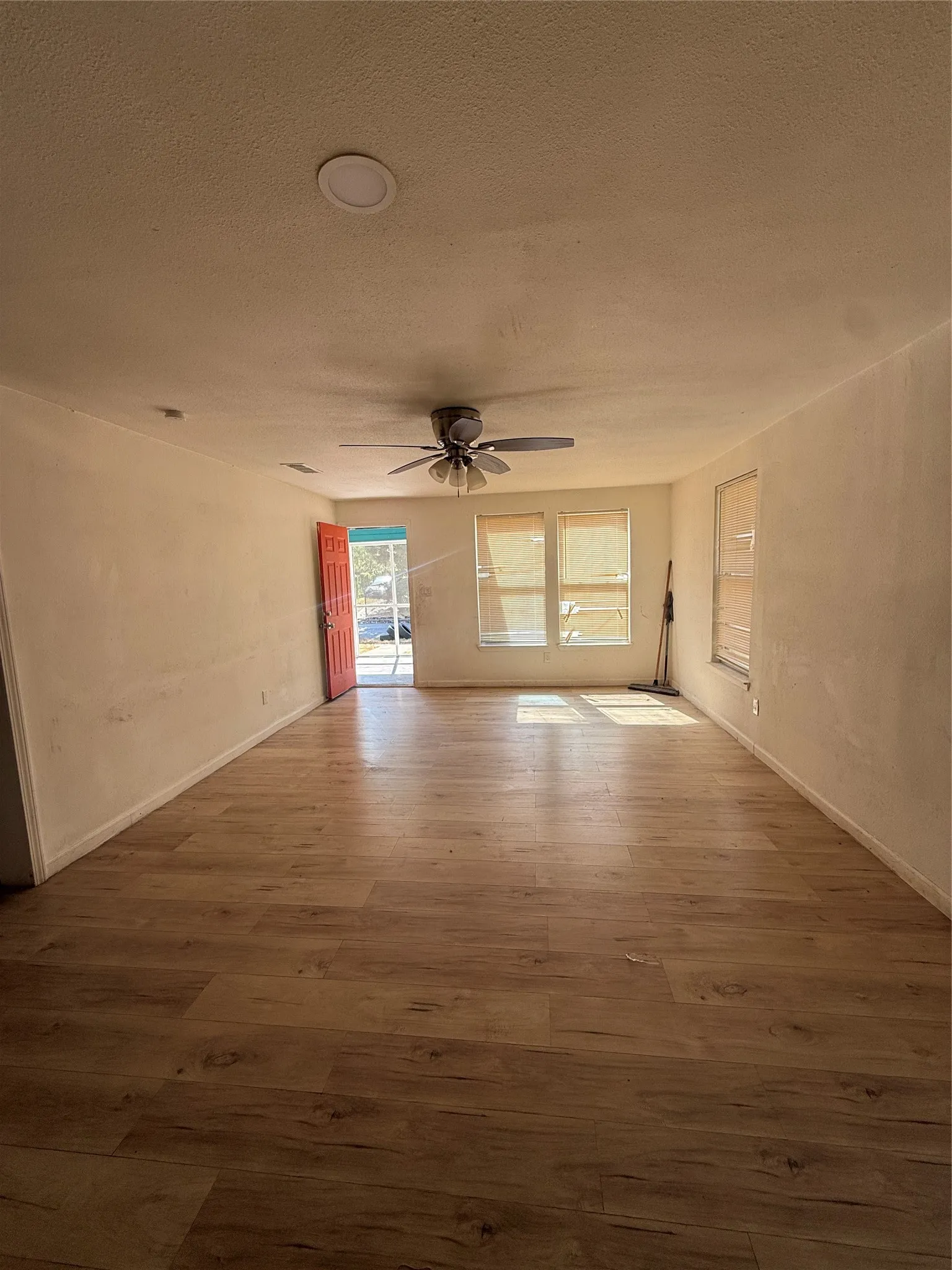 Expansive room featuring wood-finish flooring, a ceiling fan with integrated lighting, and multiple windows